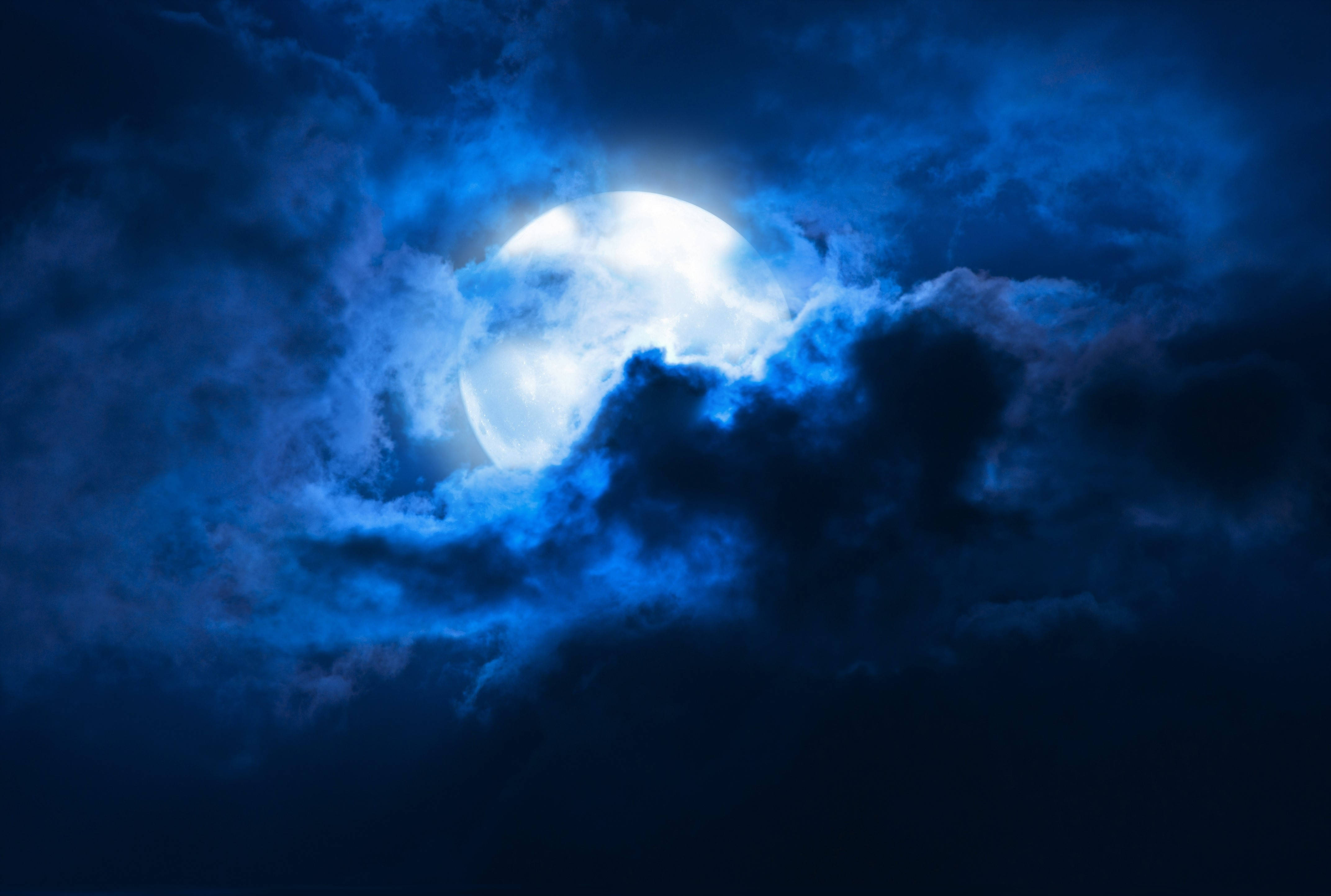 滿月隱藏於藍色雲層後 壁紙 — 一輪明亮的滿月穿透旋轉的深藍色雲層，構成戲劇性的夜空。