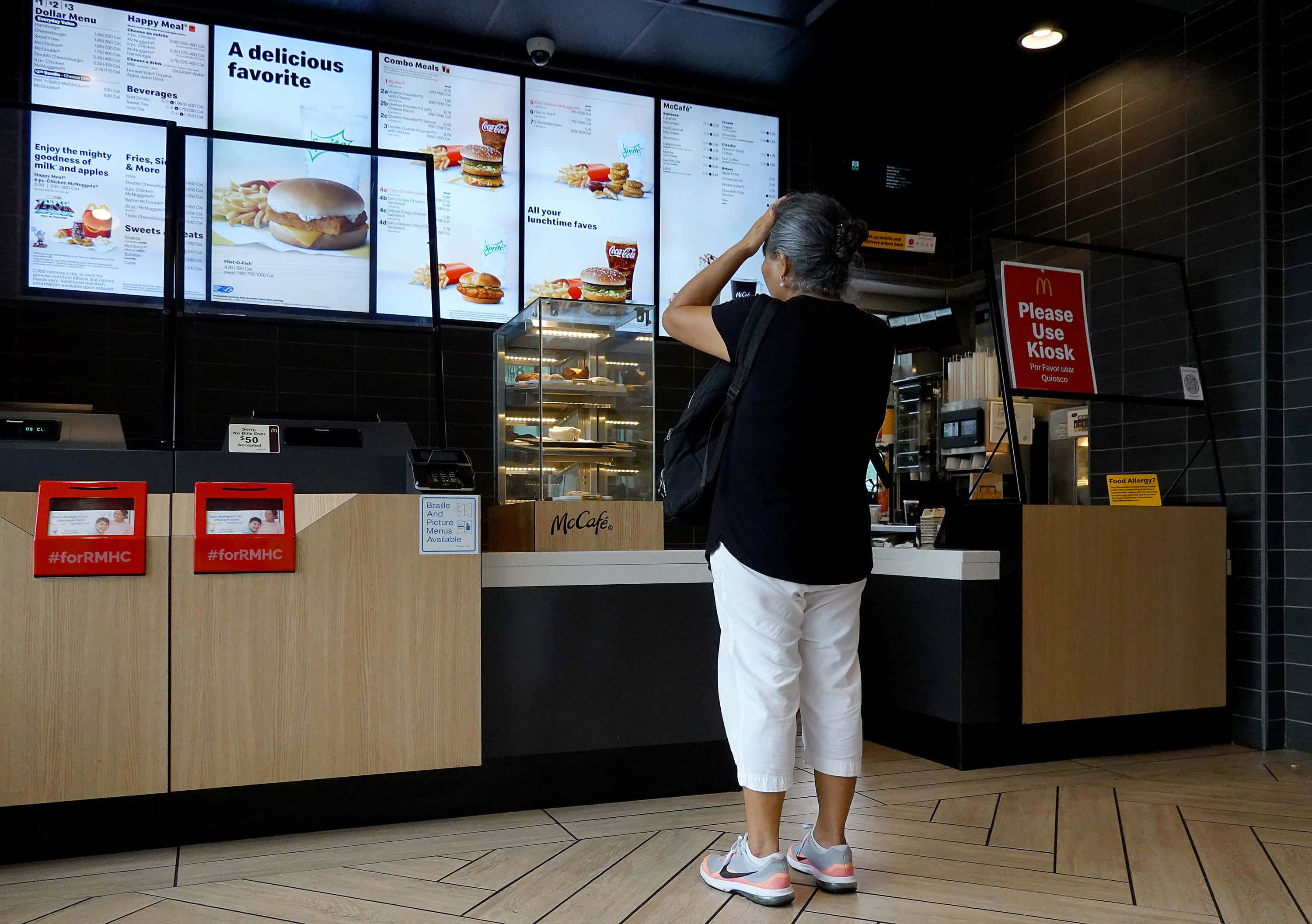 滿足所有人 cravings 的美味速食拼盤！ 壁紙 — 一位年長女性站在麥當勞餐廳內，抬頭看著顯示食品項目的數碼餐牌。