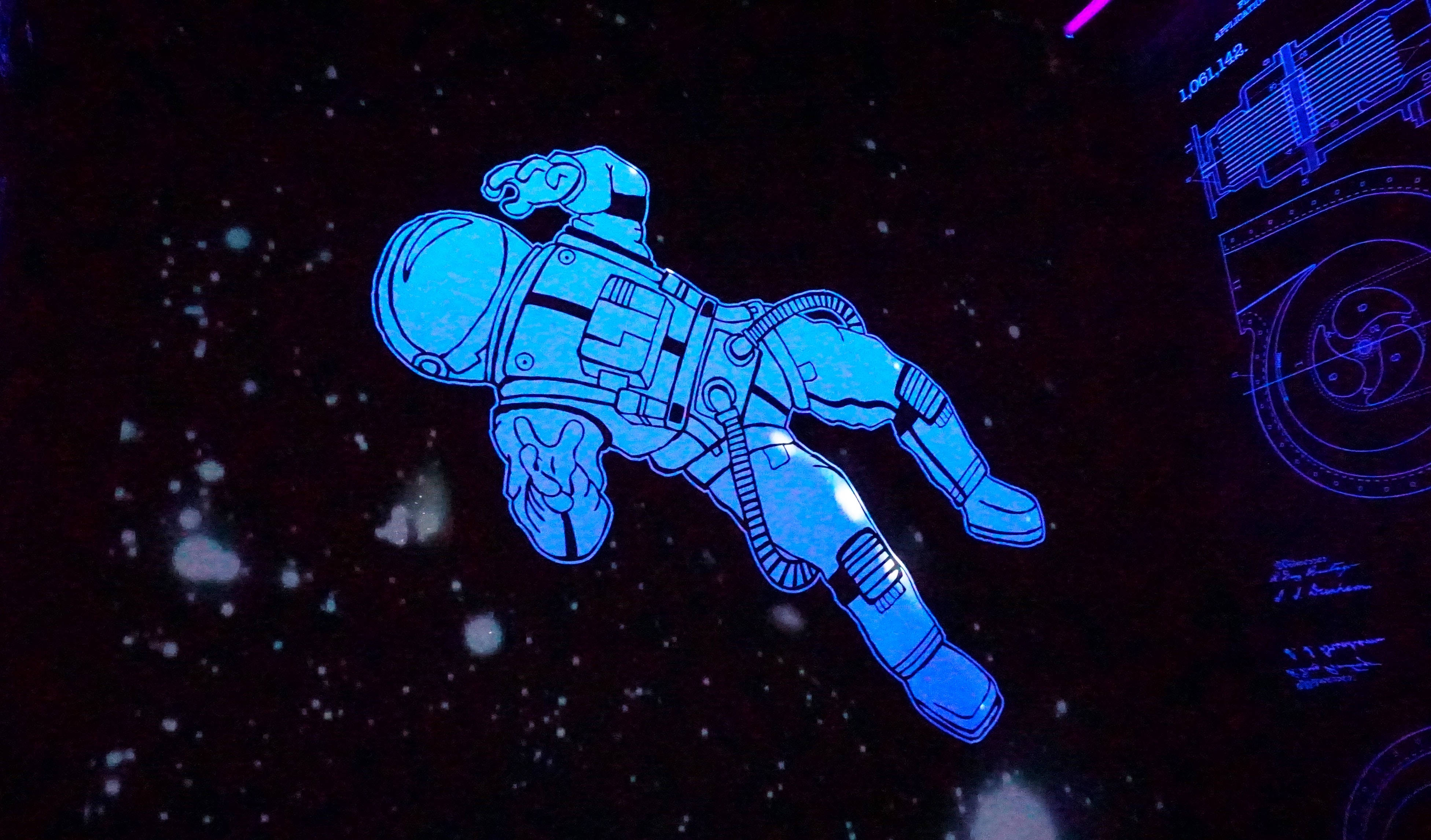 漂浮藍色宇航員動畫桌面壁紙 壁紙 — 一個發光的藍色太空人在星空黑色背景中漂浮，右側有未來感的藍色示意圖。