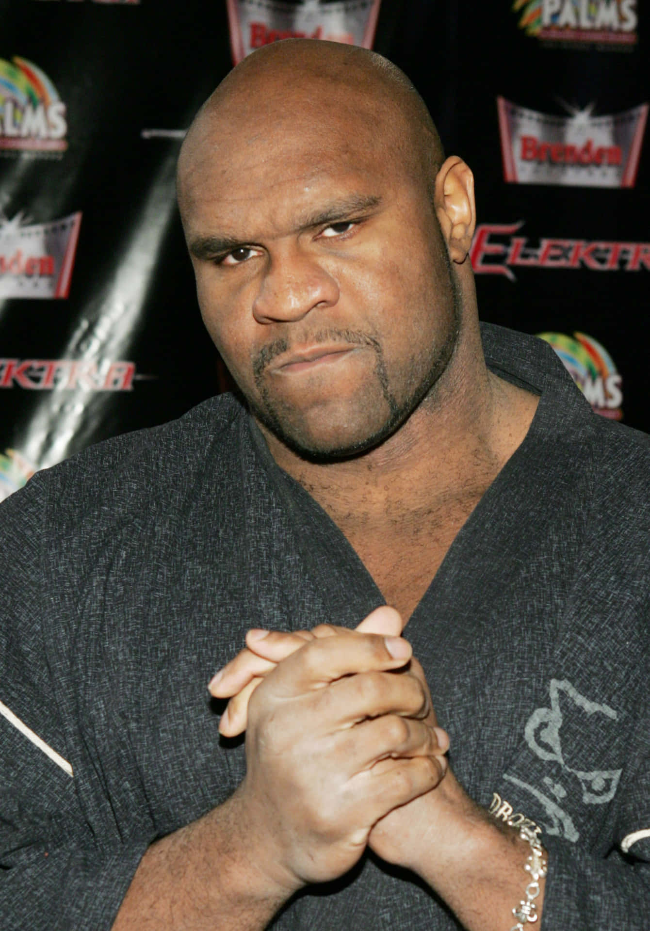 演員 Bob Sapp 壁紙 — 一個光頭男人表情嚴肅，在品牌背景前交疊雙手。