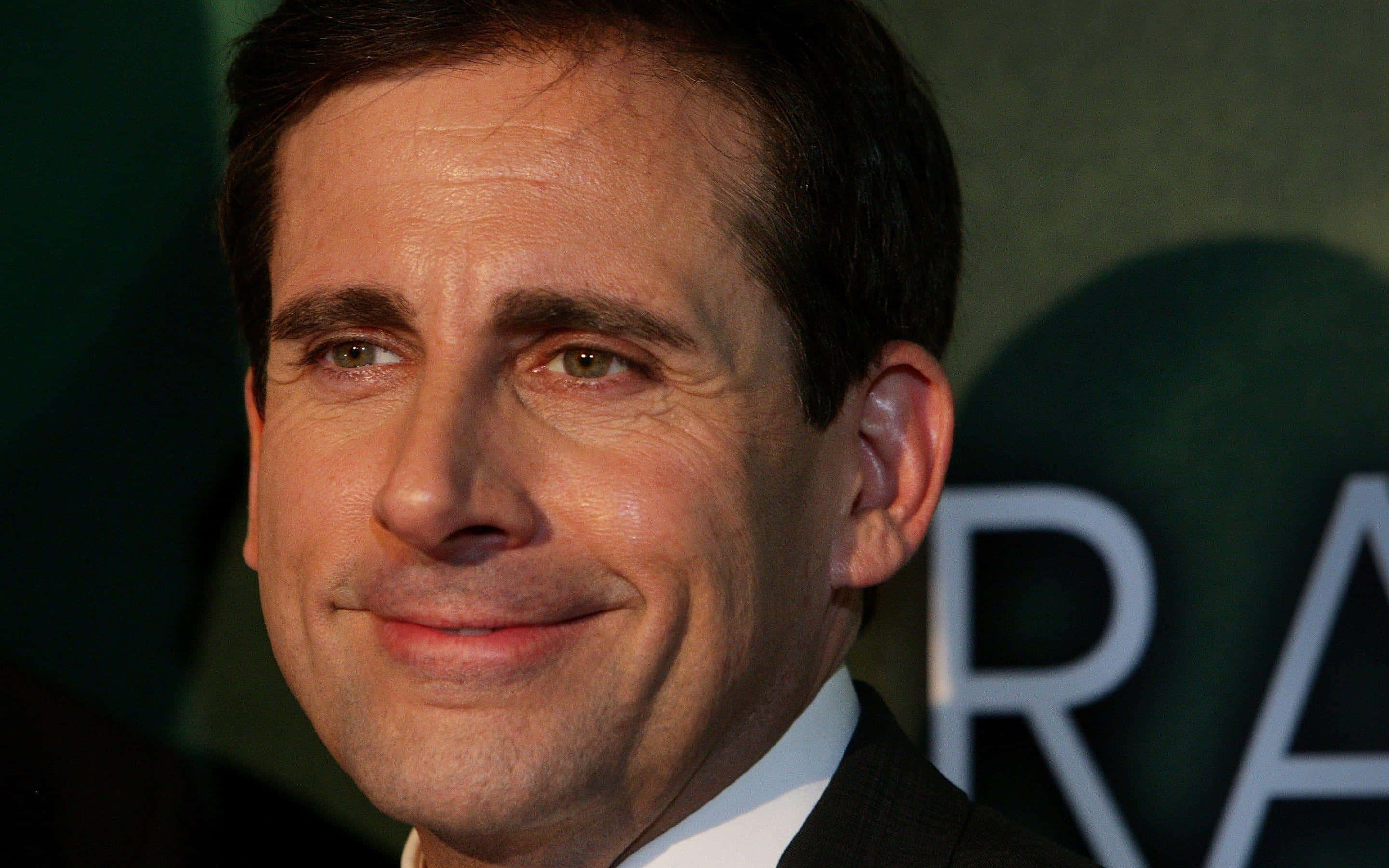 steve carell 桌布 壁紙 — 演員史提夫·加維身穿深色西裝，在模糊的綠色背景和部分白色文字前溫暖微笑的特寫肖像。