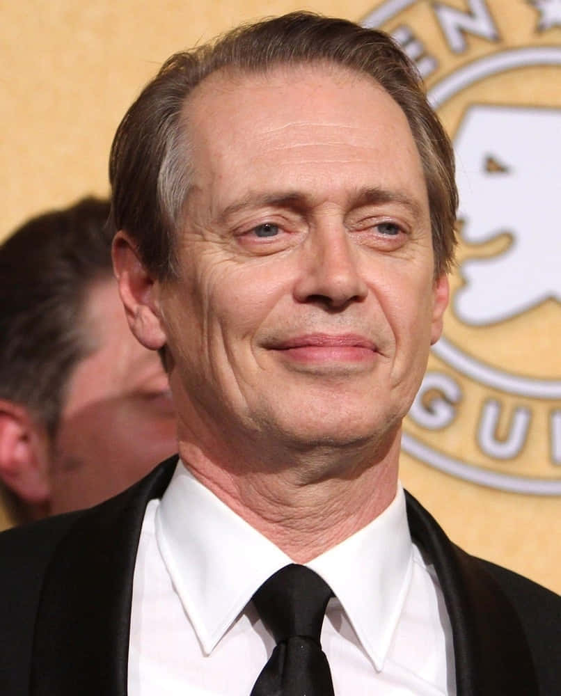steve buscemi 桌布 壁紙 — 演員史提夫·布希美在金色背景的正式活動中穿著黑色燕尾服，露出微妙的微笑。