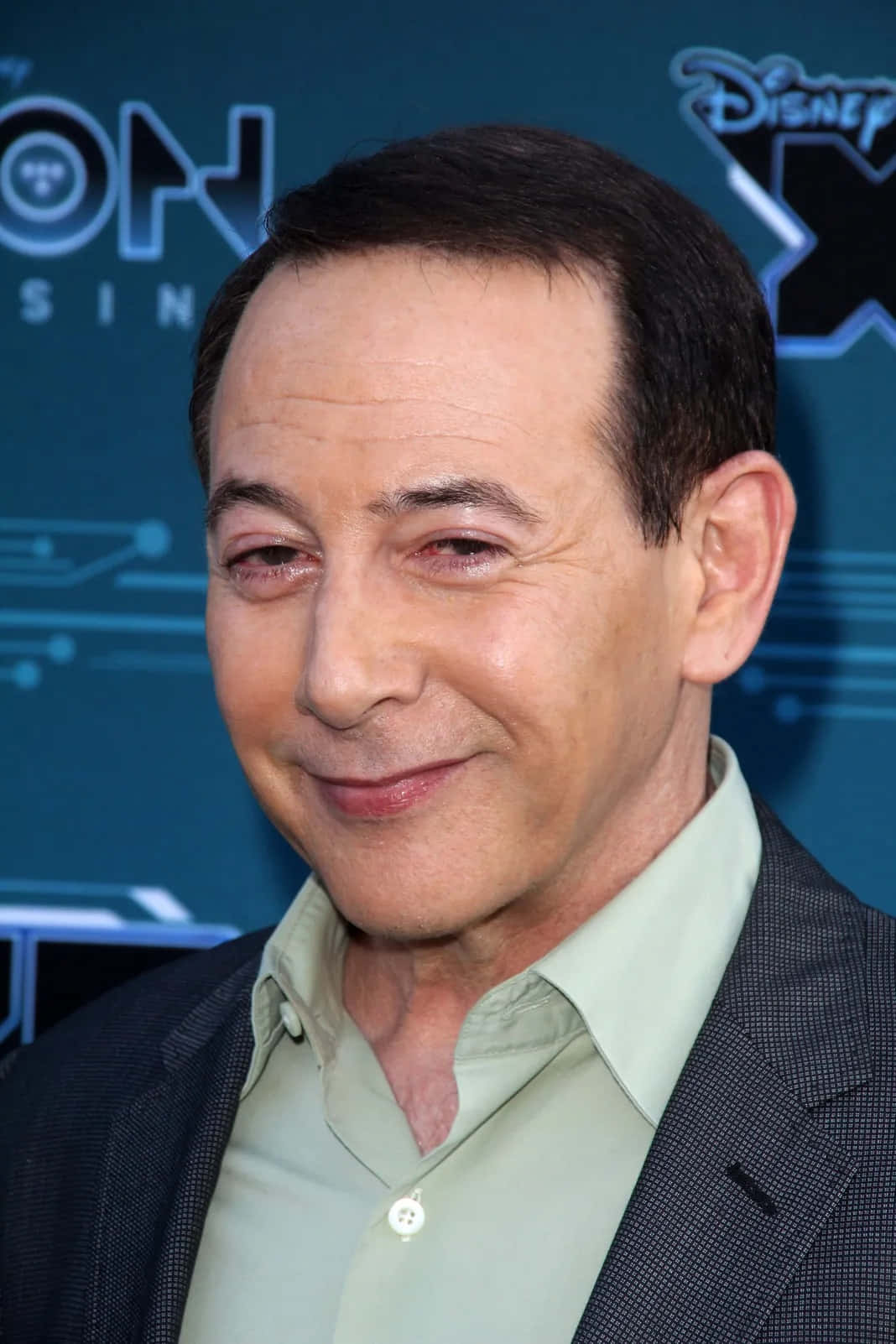 Paul Reubens 桌布 壁紙 — 演員奇雲·史柏西在迪士尼活動中穿著深色西裝和淺綠色襯衫，溫暖地微笑。