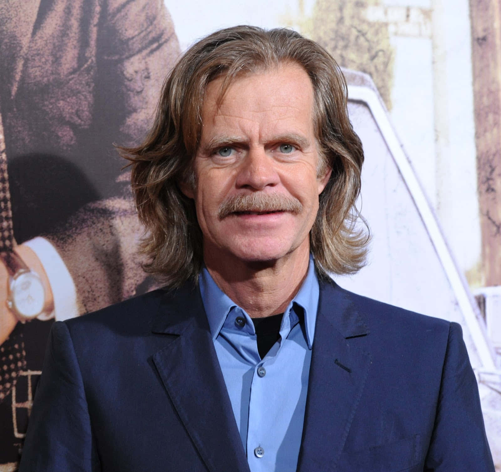 william h. macy 桌布 壁紙 — 演員威廉·H·梅西留著長波浪髮和鬍鬚，身穿海軍藍西裝和藍色襯衫出席宣傳活動。