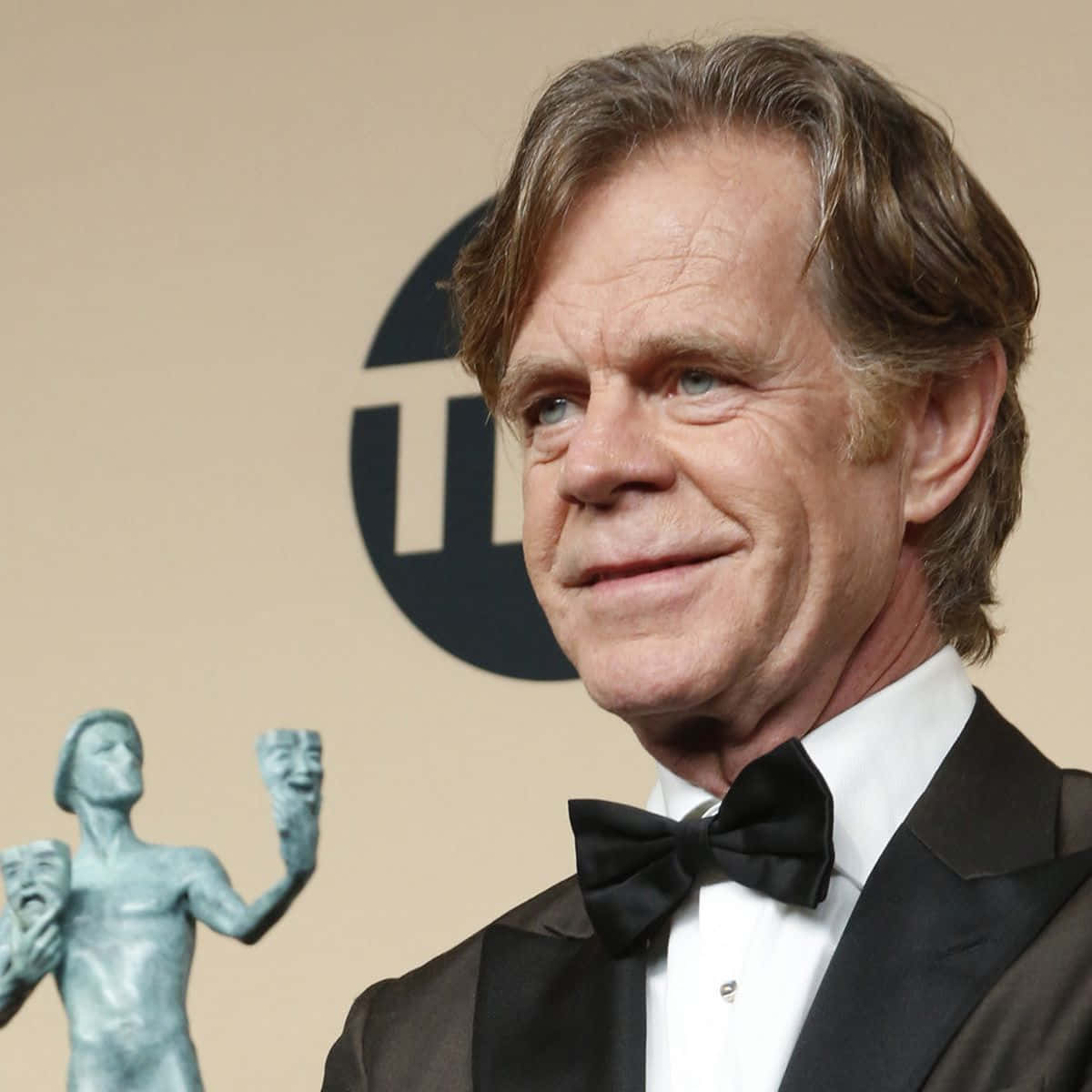 william h. macy 桌布 壁紙 — 演員威廉·H·梅西穿著黑色燕尾服配蝴蝶結，在正式活動中與劇院獎雕像旁溫暖微笑。