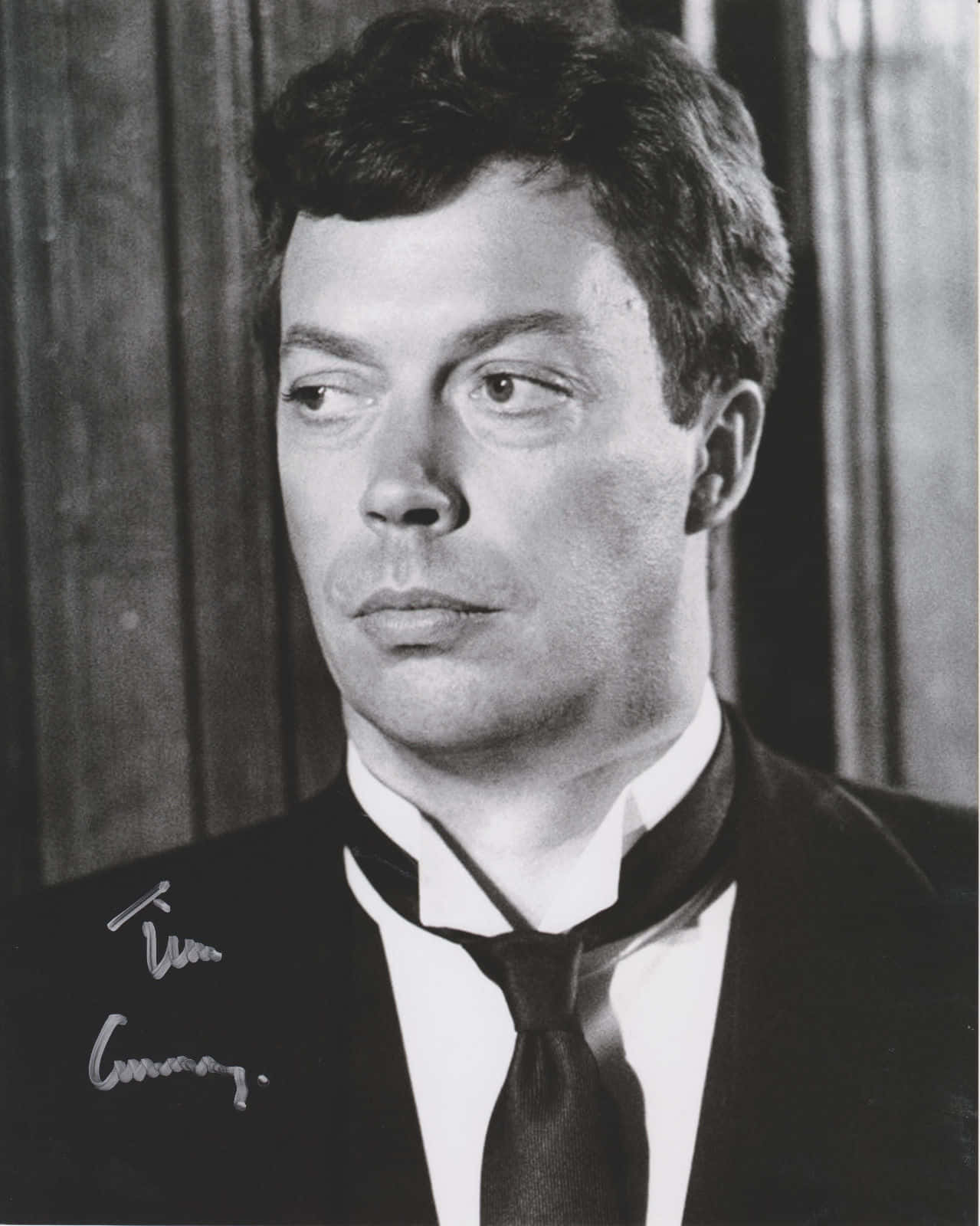 Tim Curry 桌布 壁紙 — 演員添·居里穿著西裝、表情嚴肅地望向一旁的黑白肖像。