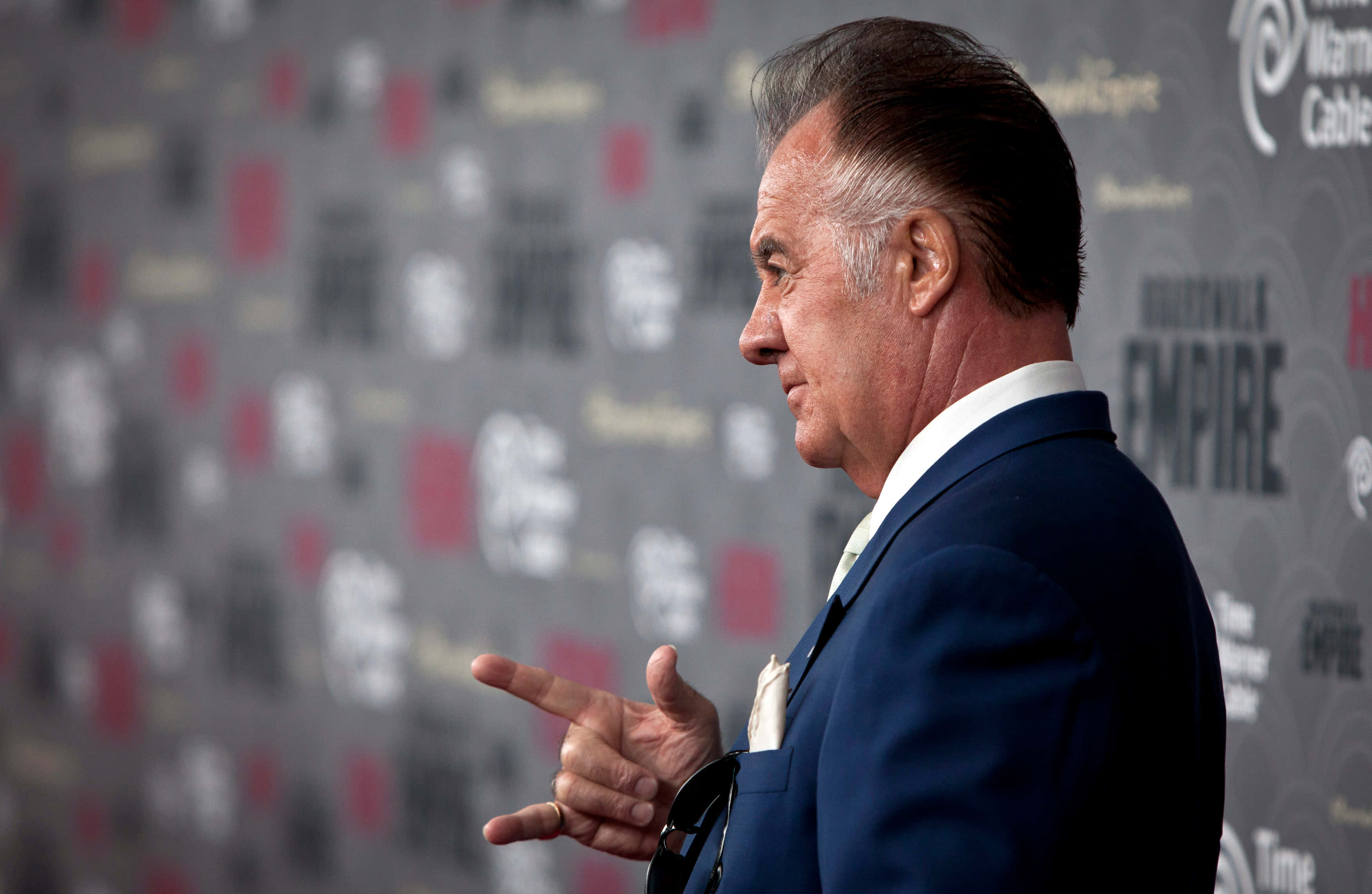 Tony Sirico 桌布 壁紙 — 演員祖·佩西身穿俐落藍色西裝，在模糊宣傳背景的紅地毯活動上自信地做手勢。