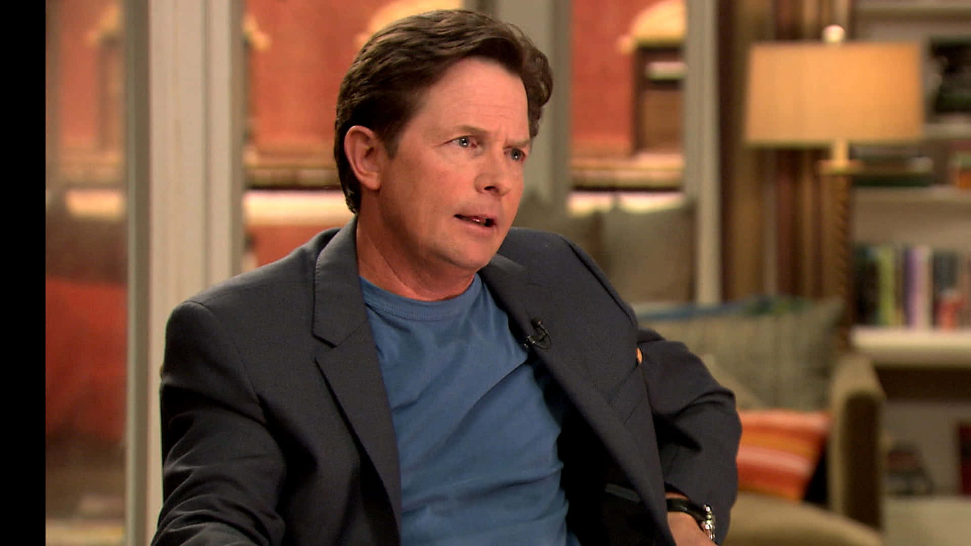 michael j fox 桌布 壁紙 — 演員米高·J·福斯在訪問期間坐在舒適的錄影室椅子上，身穿藍色T恤和深色西裝外套。