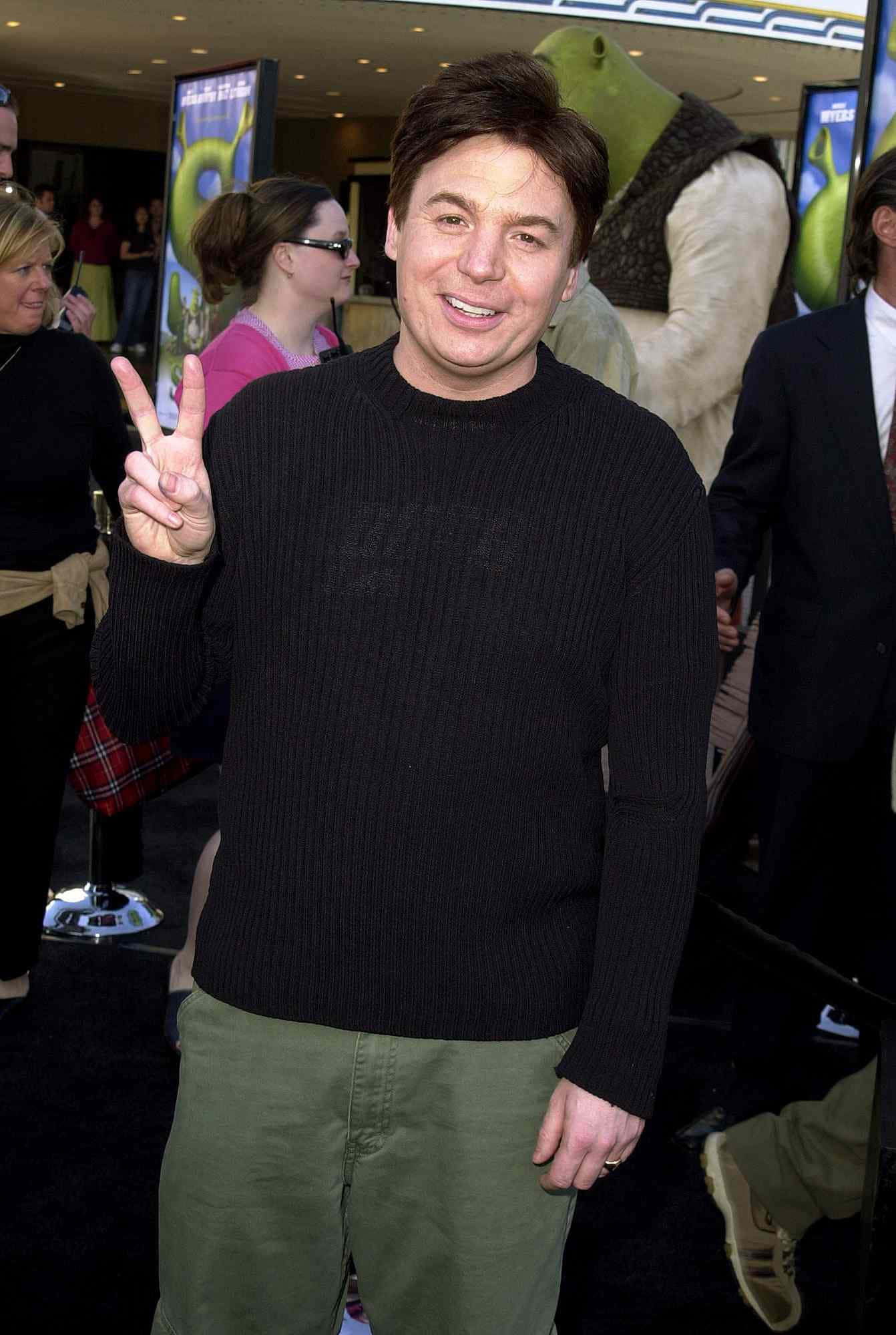 Mike Myers 桌布 壁紙 — 演員米高邁亞斯微笑並向鏡頭做出和平手勢，身後有史力加電影首映禮的綠色怪物雕像。