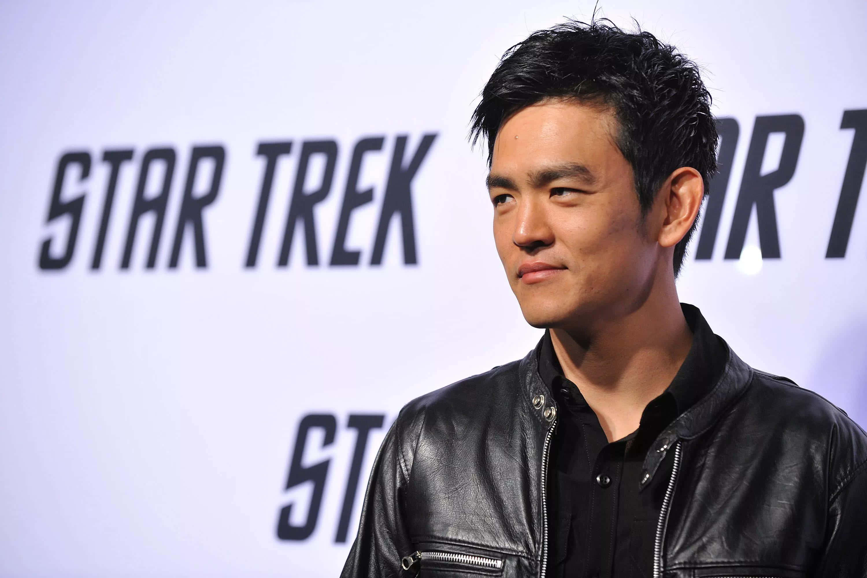 John Cho 桌布 壁紙 — 演員約翰·曹身穿黑色皮褸，自信地站在《星空奇遇記》宣傳背景前。