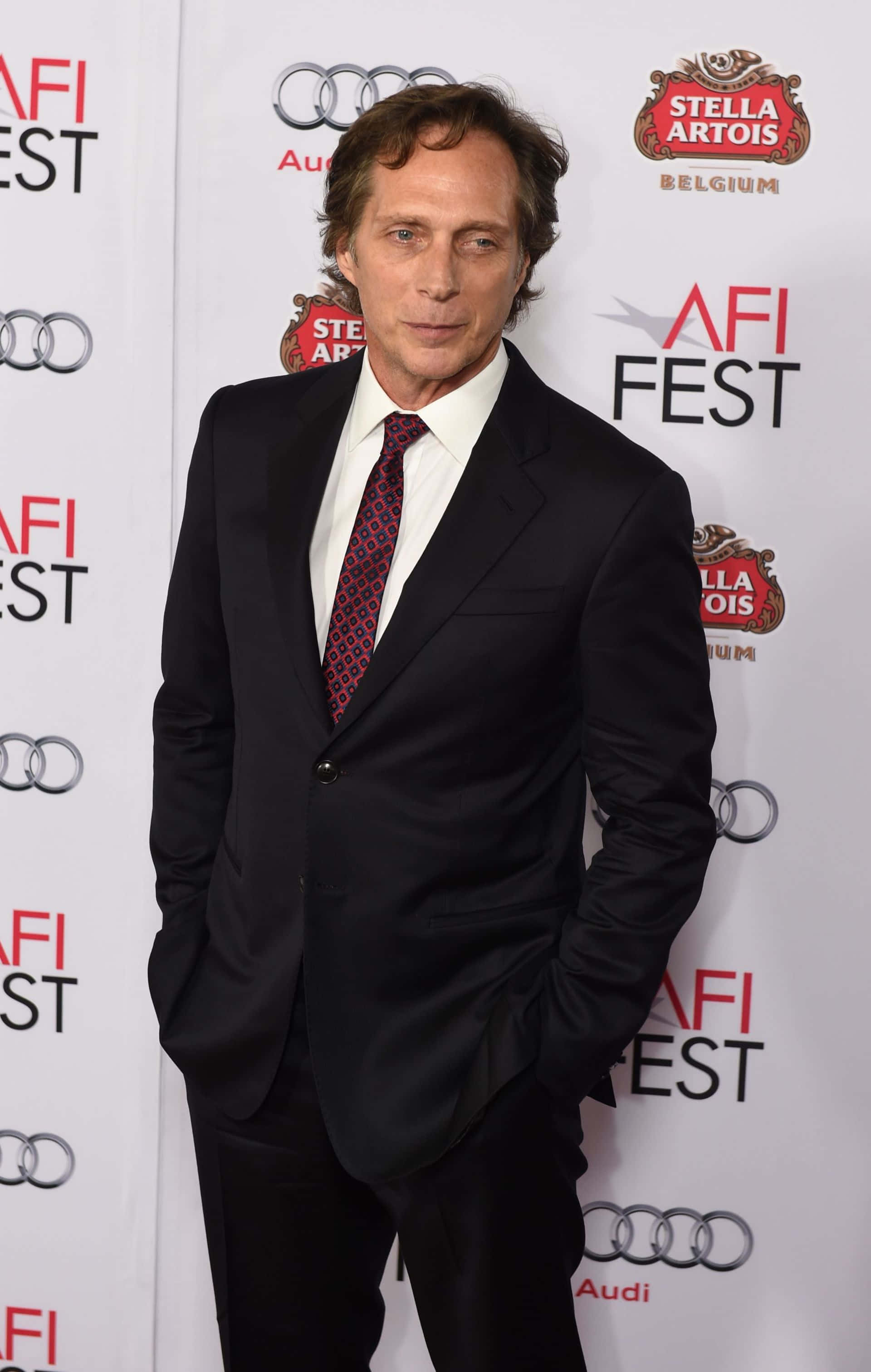 William Fichtner 桌布 壁紙 — 演員維高·莫滕森自信地站在白色背景前，身穿黑色西裝，雙手插袋，背景上有AFI FEST Audi和Stella Artois標誌。