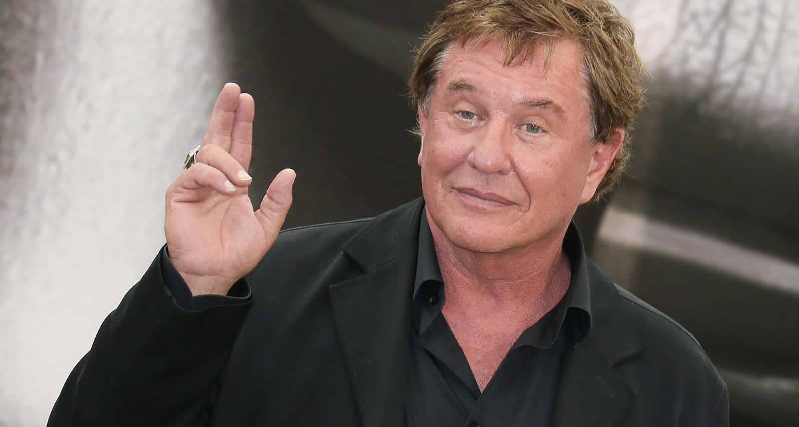 Tom Berenger 桌布 壁紙 — 演員韋基馬穿著黑色西裝和襯衫，比出和平手勢揮手。
