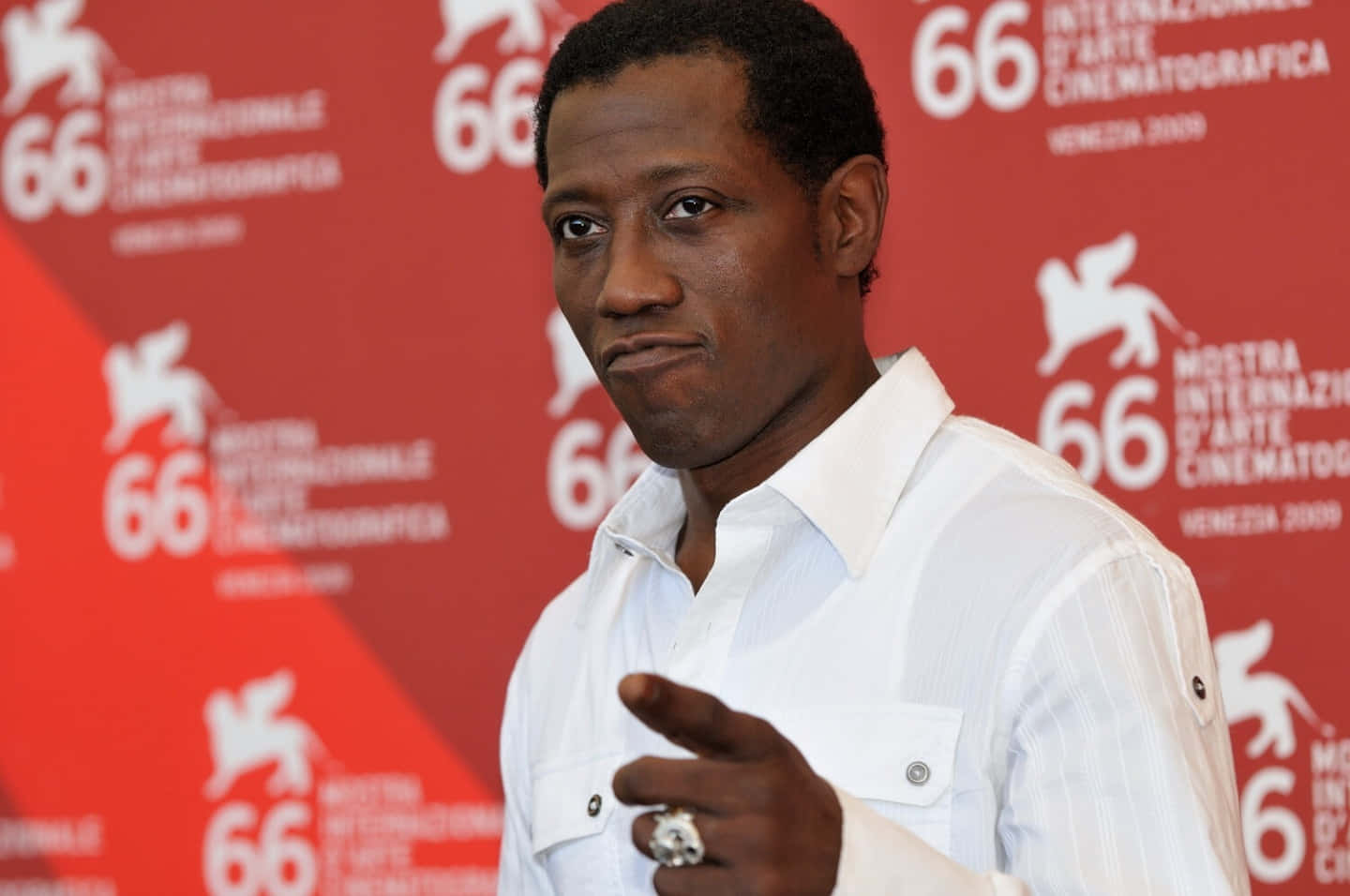 Wesley Snipes 桌布 壁紙 — 演員韋斯利·斯奈普斯在第66屆威尼斯電影節上自信地擺姿勢，身穿白色襯衫，戴著戒指的手做手勢，背景為紅色品牌背景。