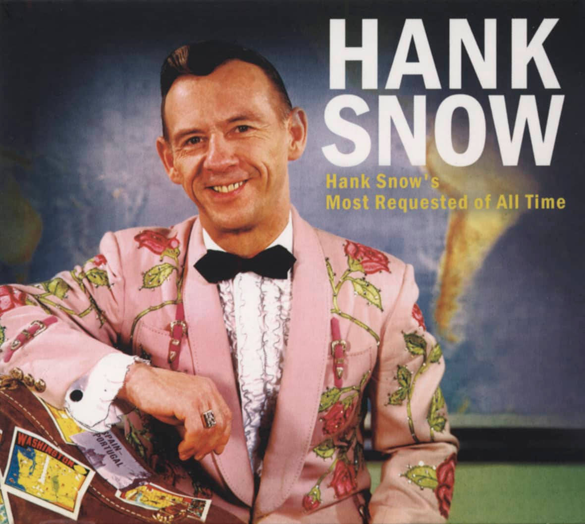 漢克·斯諾歷來最受歡迎歌曲海報 壁紙 — Hank Snow 身穿粉紅色玫瑰刺繡西裝，微笑著拿著一個貼有旅行貼紙的手提箱。