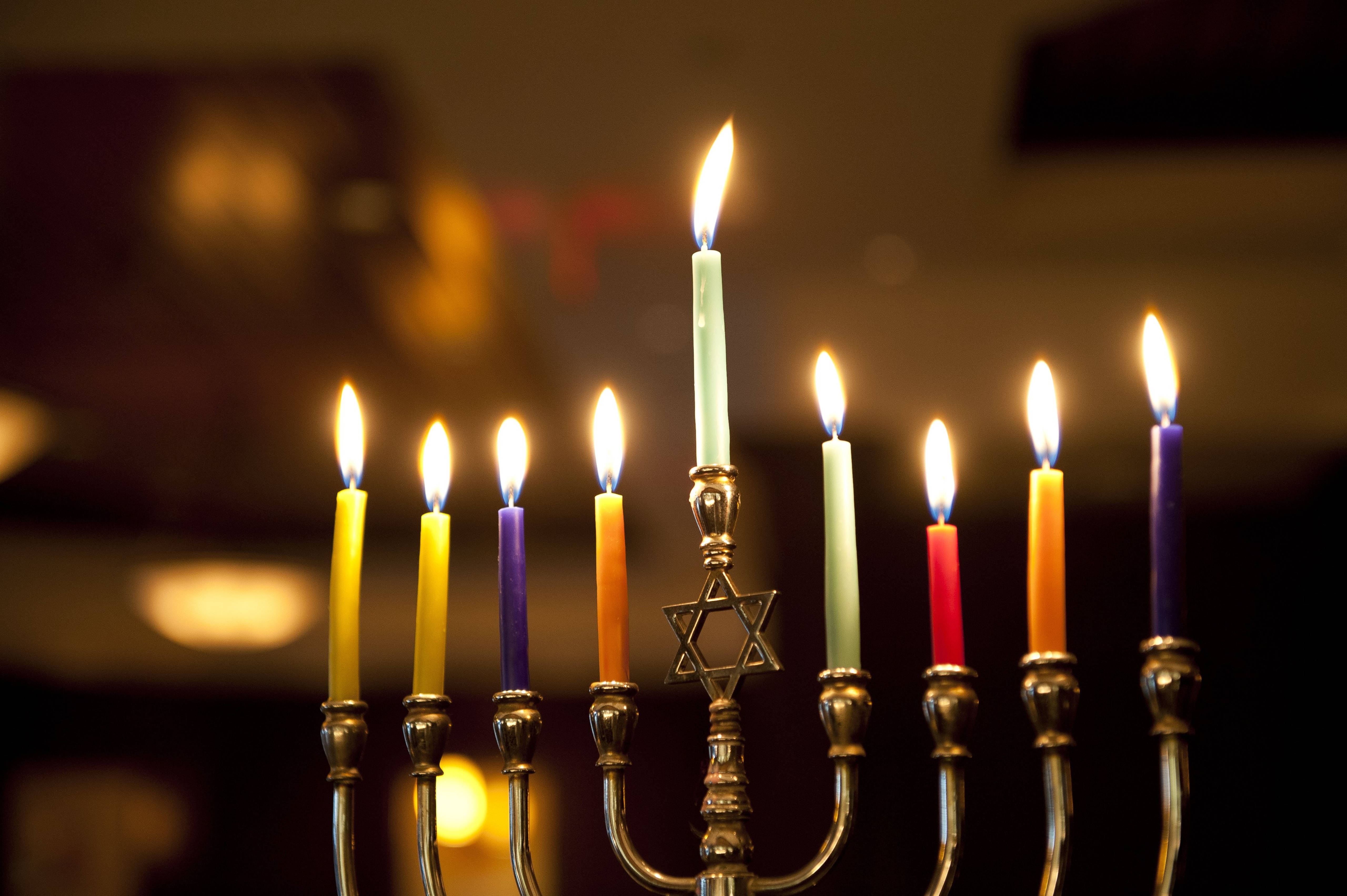 漢克節燭台節日 壁紙 — 一個點燃的九枝彩色蠟燭的 menorah 特寫，在黑暗模糊的背景中溫暖地發光。