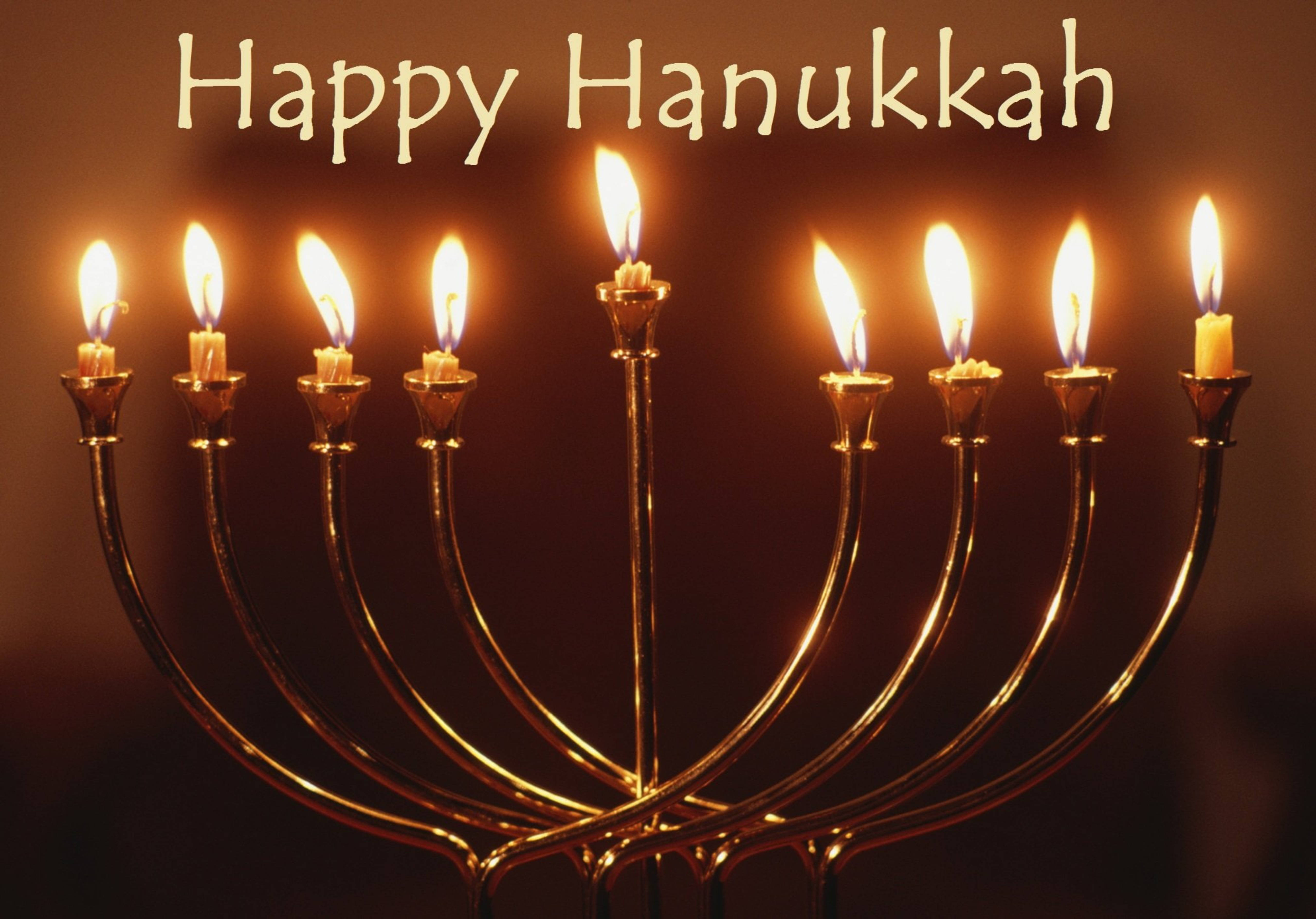 漢克節燭台金屬風格 壁紙 — 金色 menorah 上有八枝點燃的蠟燭和中央的 shamash，在黑暗背景中溫暖發光，並有「Happy Hanukkah」文字。