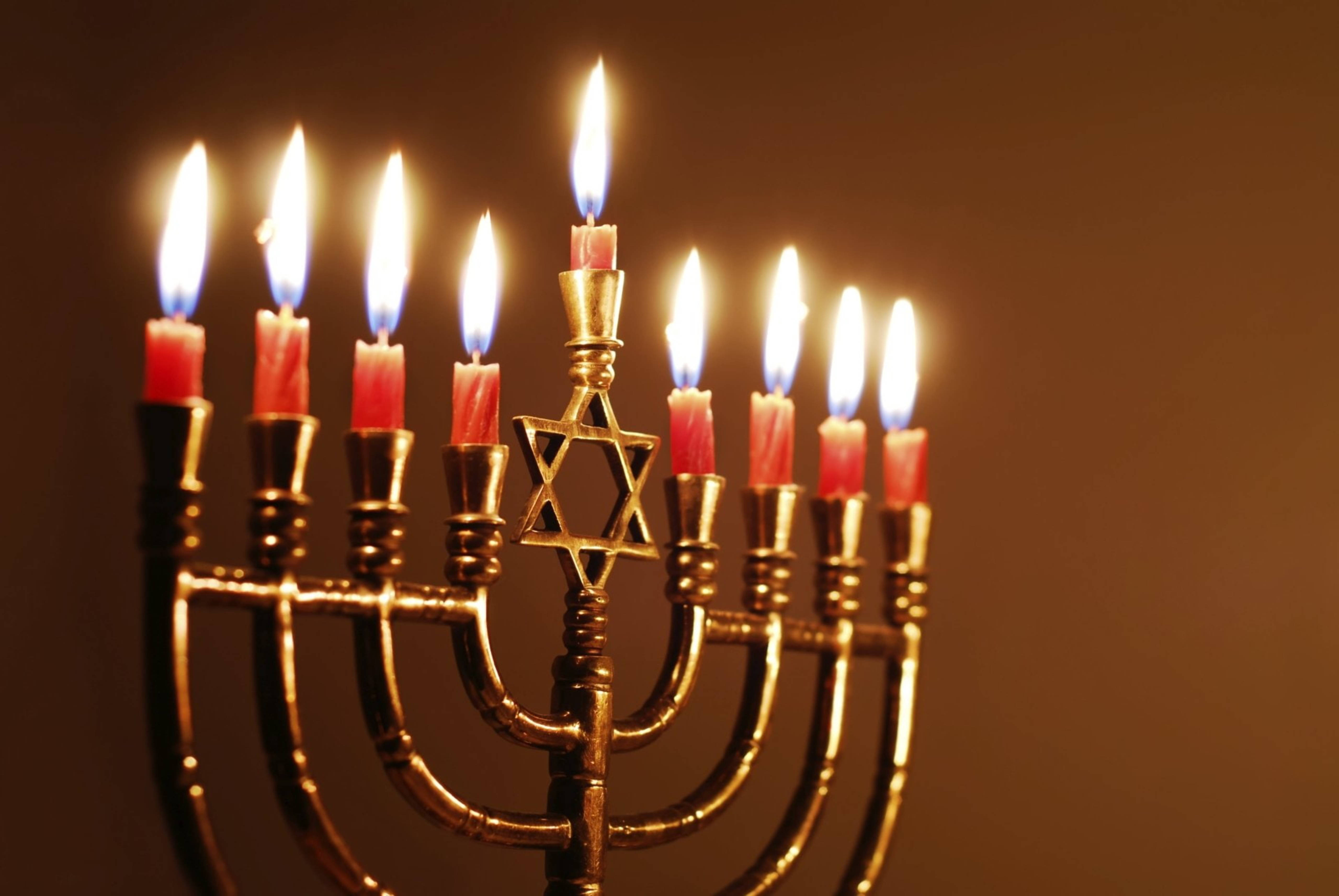 漢克節節日燭台 壁紙 — 一個金色的九枝紅色蠟燭點燃的 menorah，在深棕色背景上散發出溫暖的光芒。