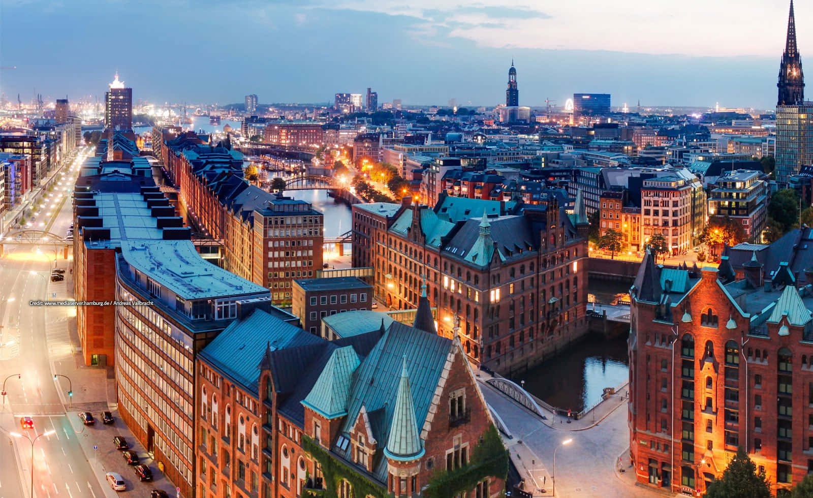 Germany 桌布 壁紙 — 漢堡歷史港口的黃昏航拍圖，發光的街燈和亮燈的磚建築倒映在平靜的水面上。