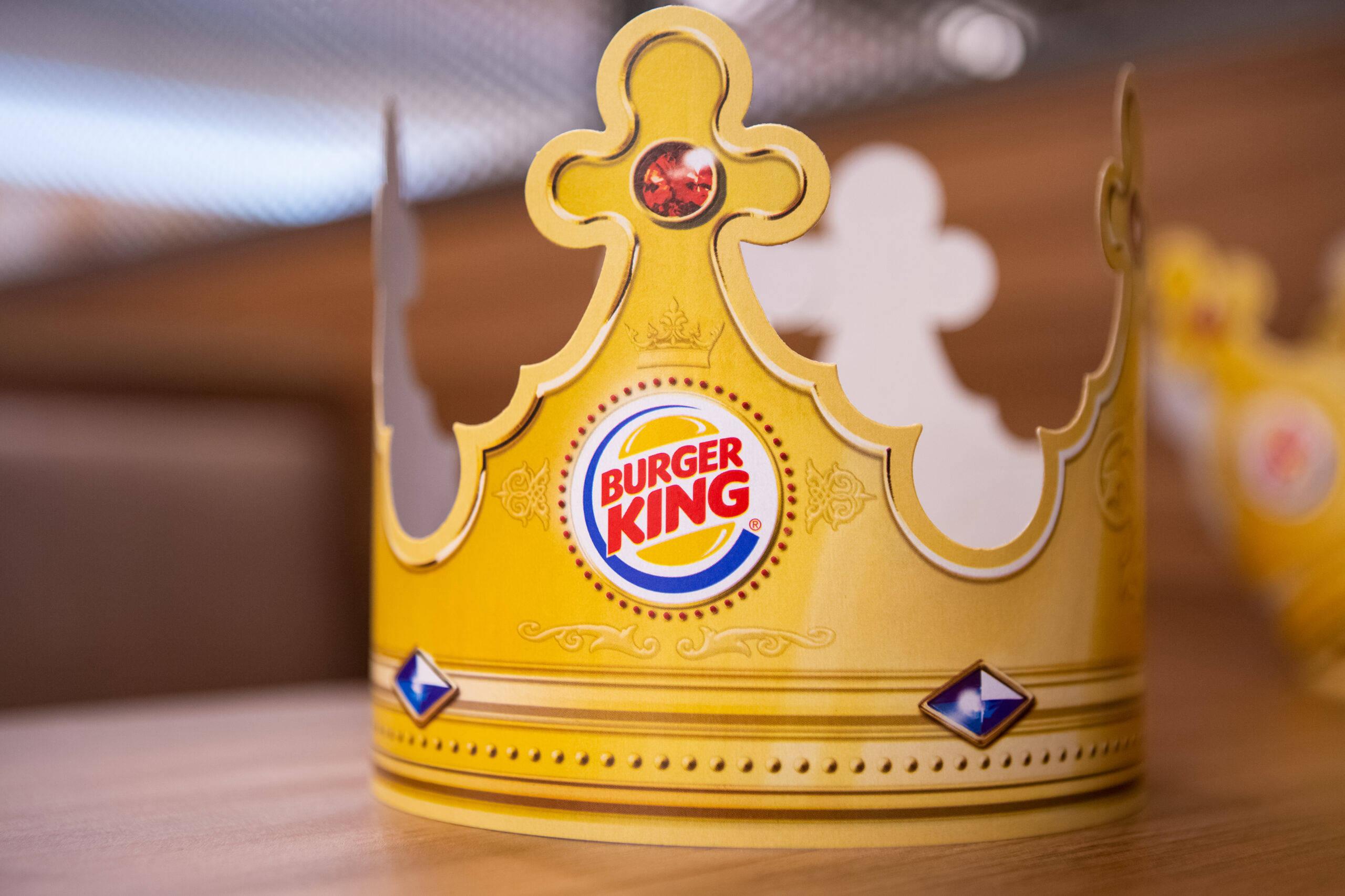 漢堡王派對帽 壁紙 — 一個帶有紅色寶石的金色Burger King皇冠放在溫暖燈光的餐廳木桌上。