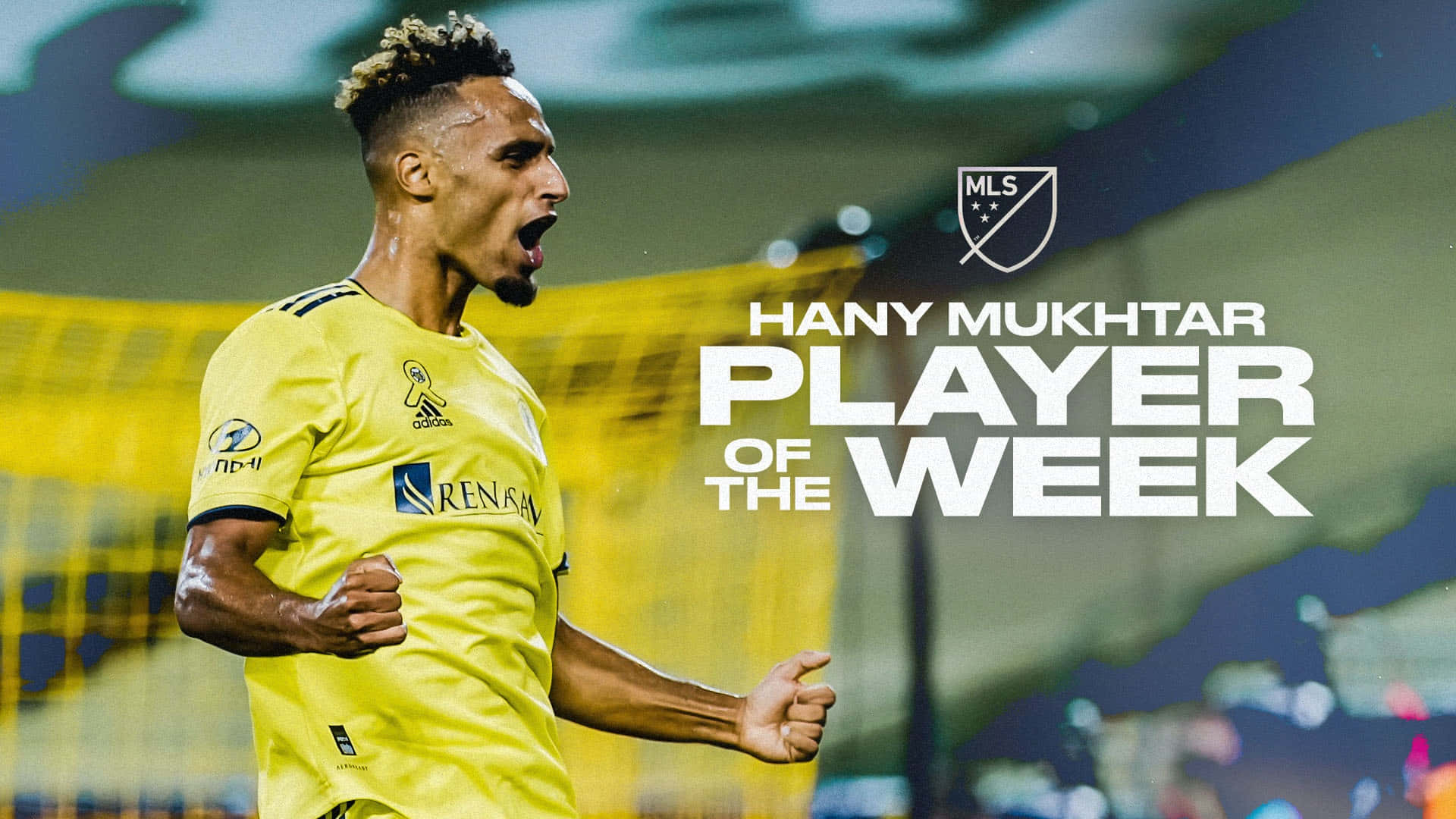 漢尼·穆克塔爾 MLS 週度最佳球員第23週 壁紙 — 一名身穿黃色球衣的足球員在球場燈光下握緊拳頭熱情慶祝。