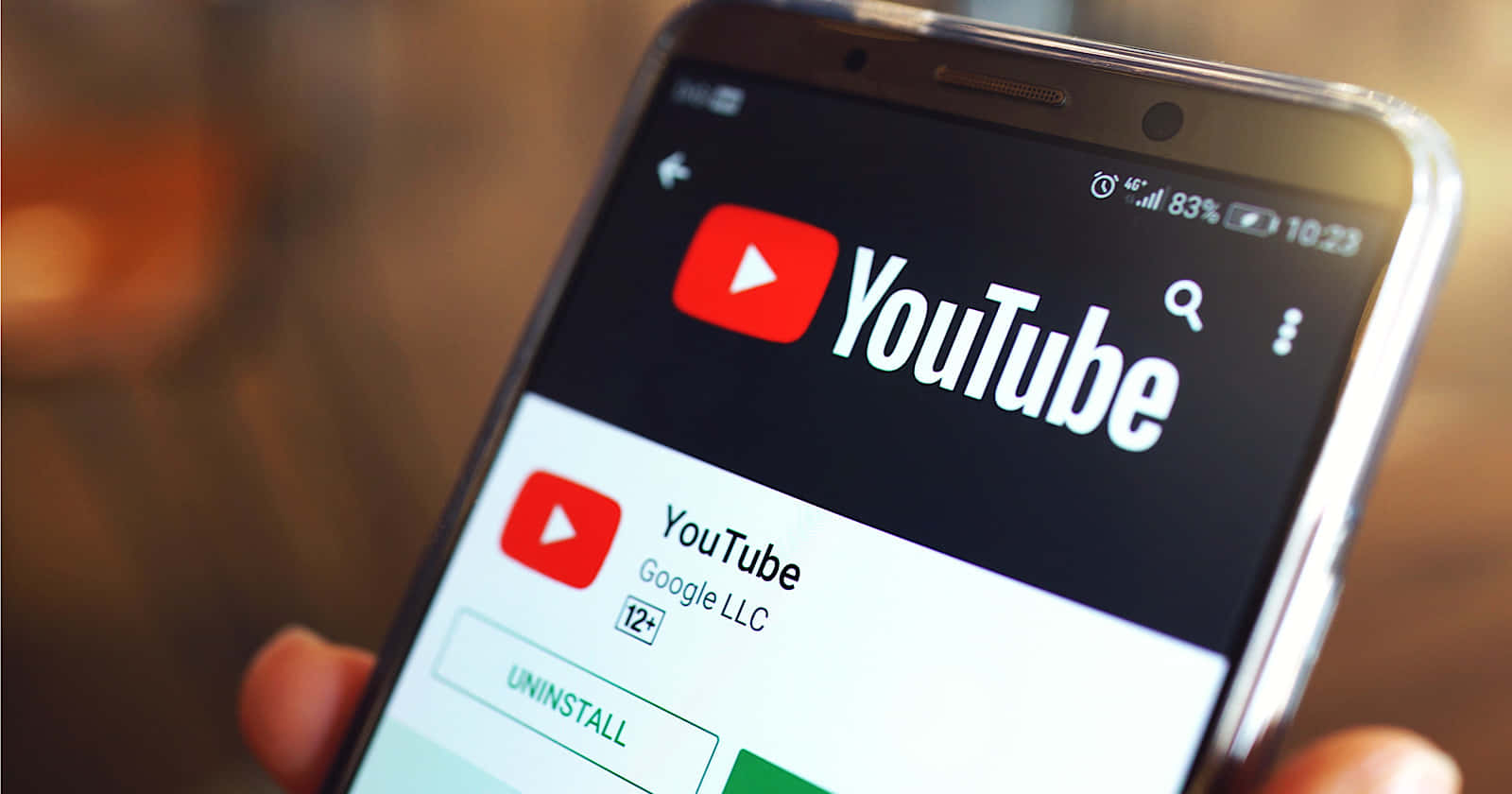 潛入 YouTube 的世界 壁紙 — 特寫一隻手拿著智能手機，顯示 YouTube 應用程式商店頁面，應用程式圖示和解除安裝按鈕可見。