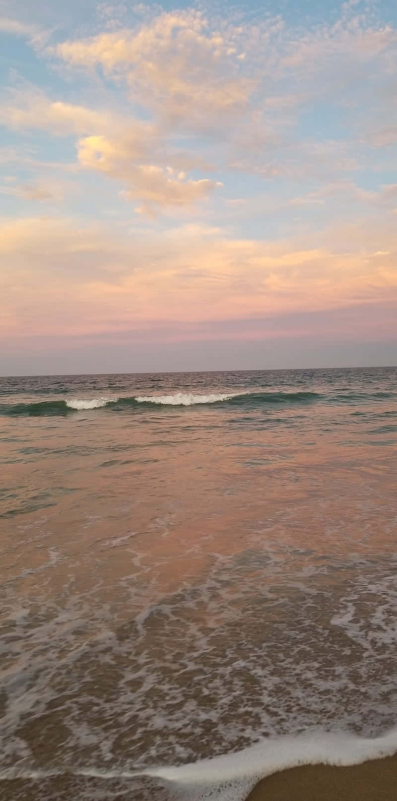 夕陽下的海浪，粉紅色和藍色的天空倒映在水面上。