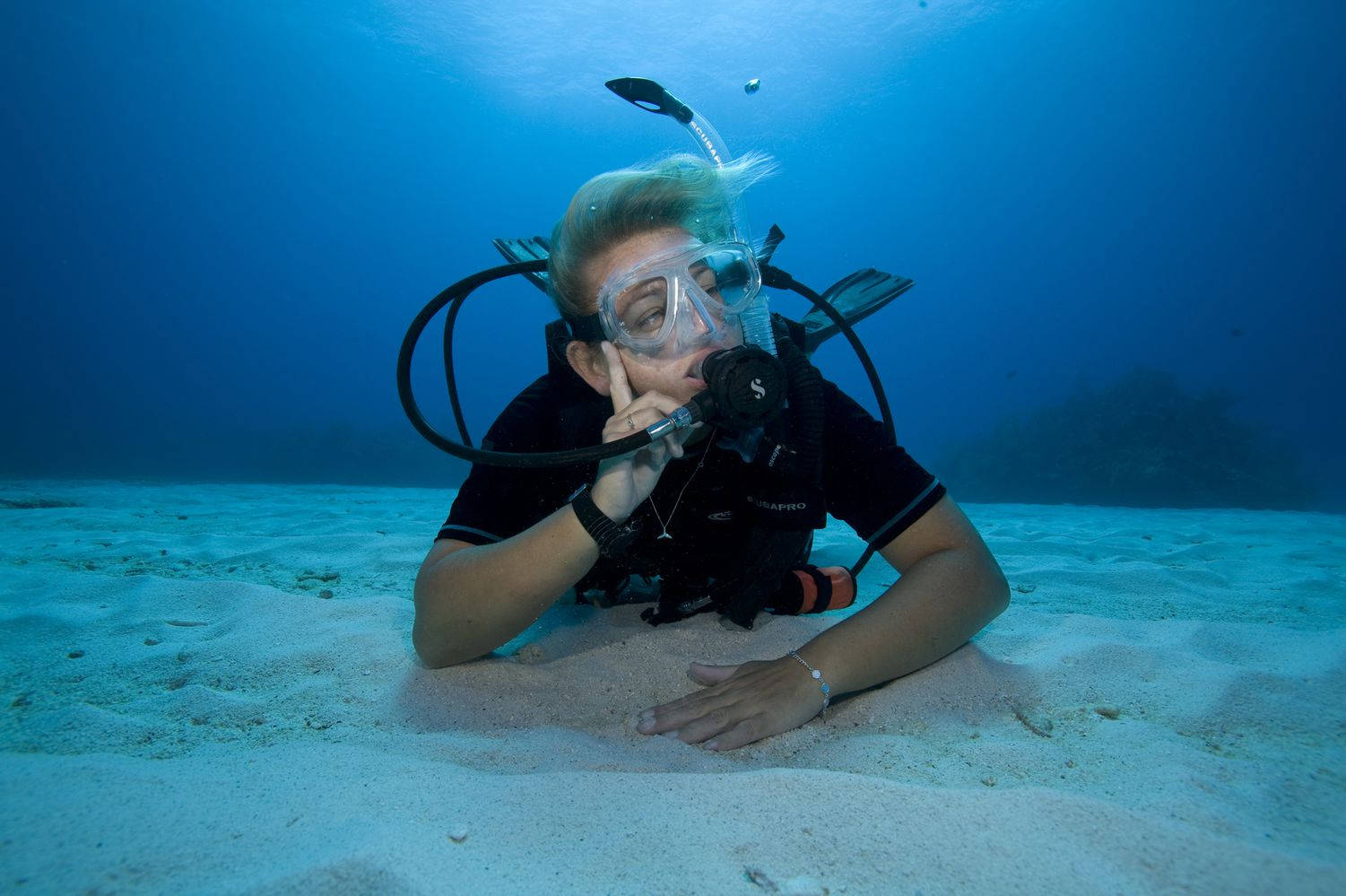 水肺潛水員在沙質海床上休息，仰望過濾的陽光。