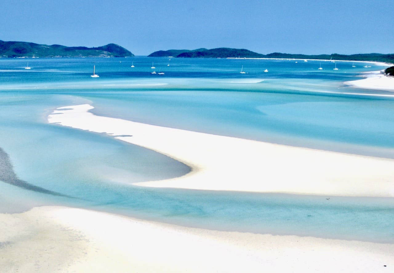 澳洲惠特桑迪群島 壁紙 — 一條純淨的白色沙洲蜿蜒穿過晶瑩剔透的碧綠海水，點綴著帆船，在明亮的藍天下。