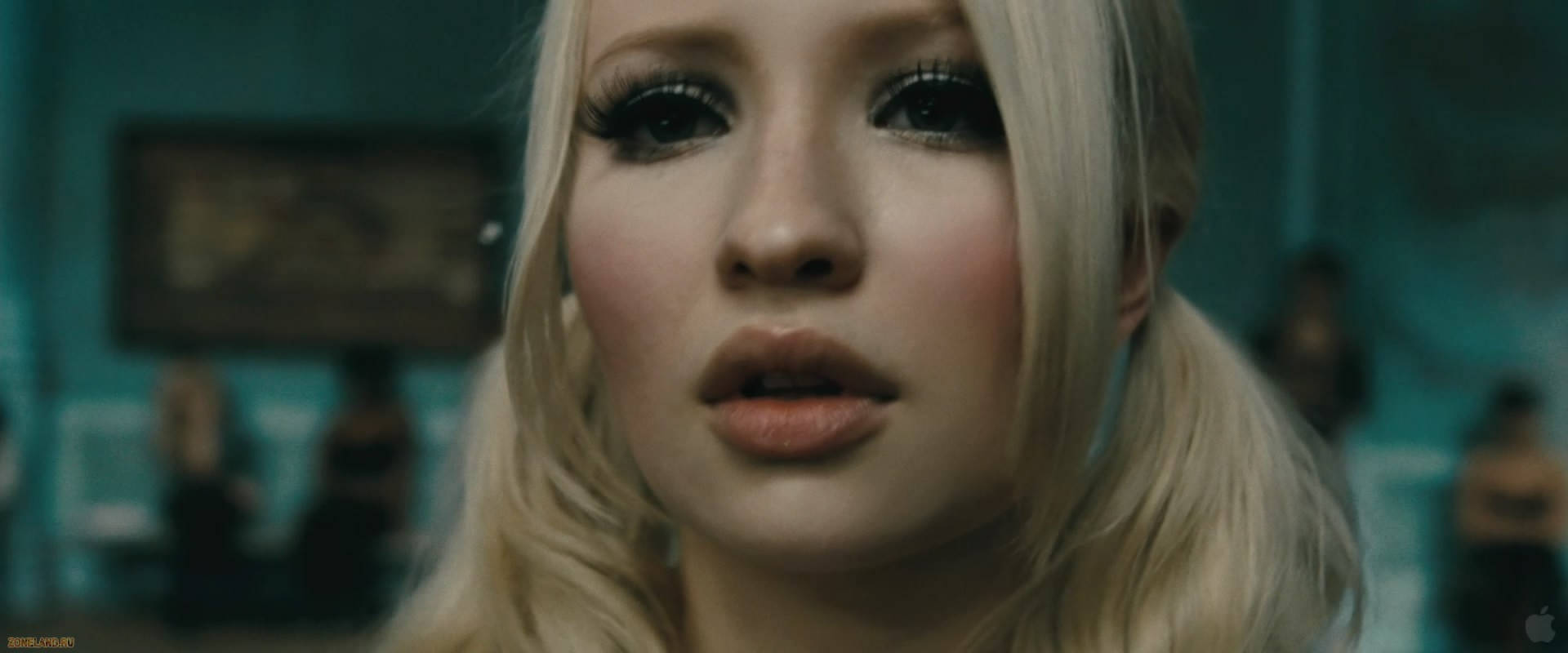 澳洲時尚模特兒艾米莉·布朗寧飾演《Sucker Punch》中的Baby Doll（2011） 壁紙 — 特寫鏡頭：一位金髮女子化著戲劇性妝容，在青綠色燈光的房間內向前望，身後有模糊的人影。