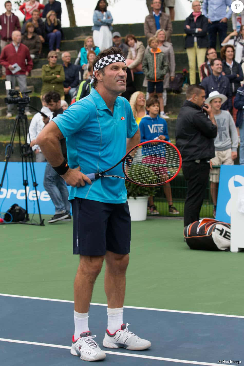 澳洲男孩 Pat Cash 壁紙 — 一名身穿藍色襯衫和格子頭帶的男網球選手站在綠色球場上，手持紅色球拍，背景有觀眾。