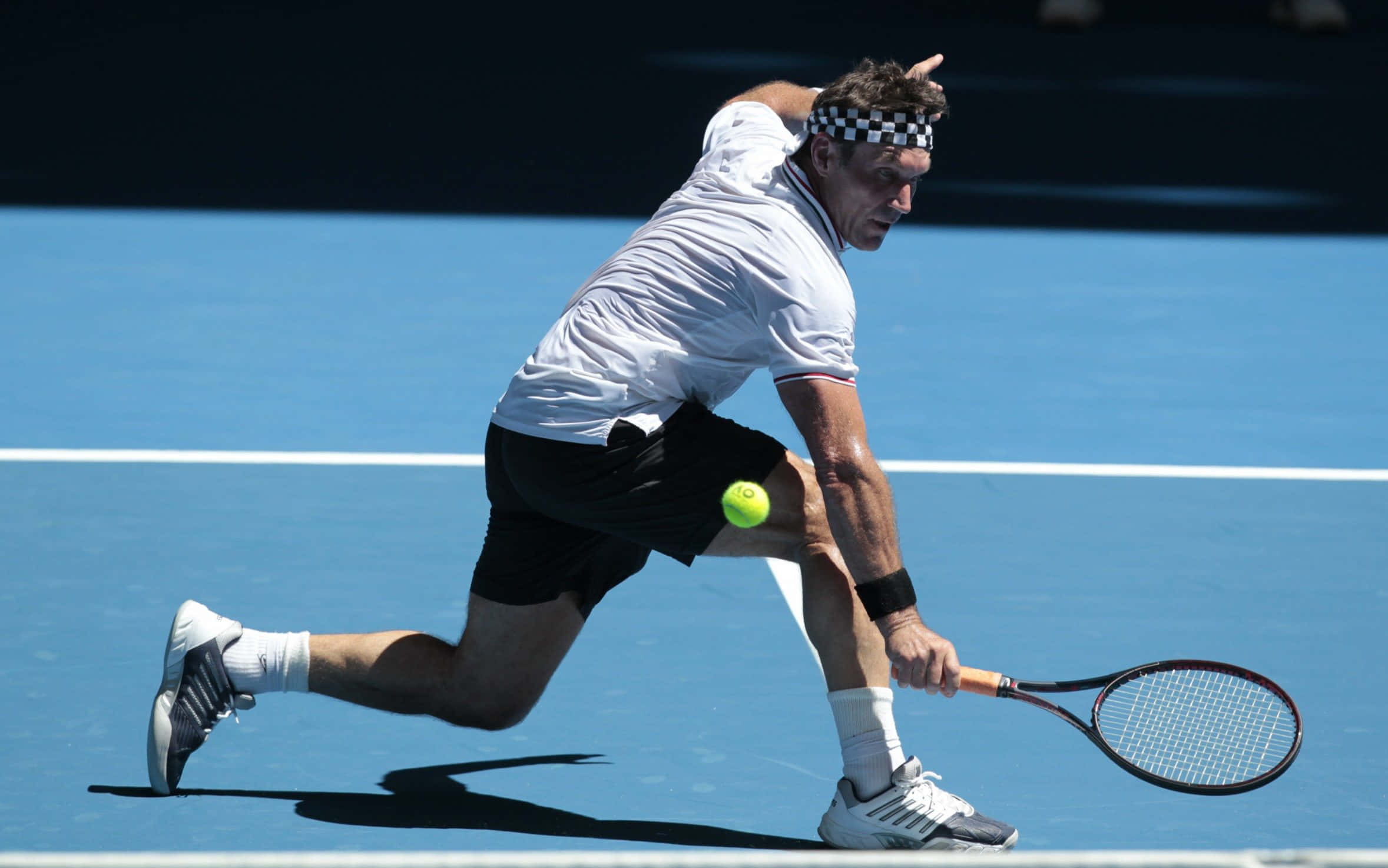 澳洲網球選手 Pat Cash 練習照 壁紙 — 一名男性網球運動員在藍色球場上低身撲出，以強烈的專注力和運動力量猛擊黃色球。