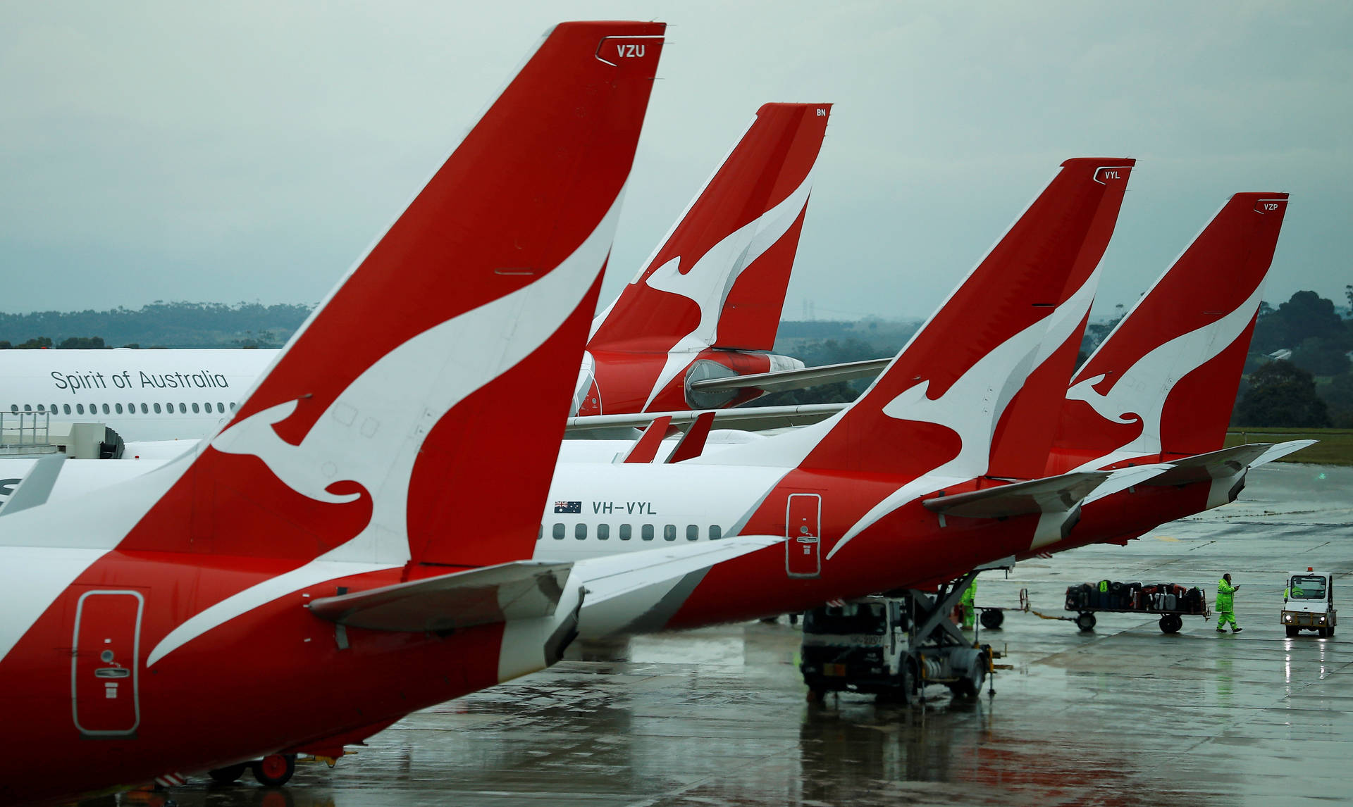 四架澳洲航空飛機停在濕滑的停機坪上，附近有地勤人員。