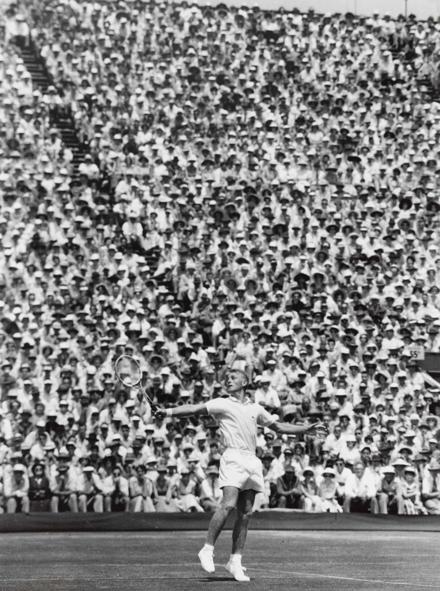 澳洲運動員萊·霍德1956年戴維斯盃賽事 壁紙 — 一位網球運動員在擠滿戴白帽觀眾的體育館中正準備發球。