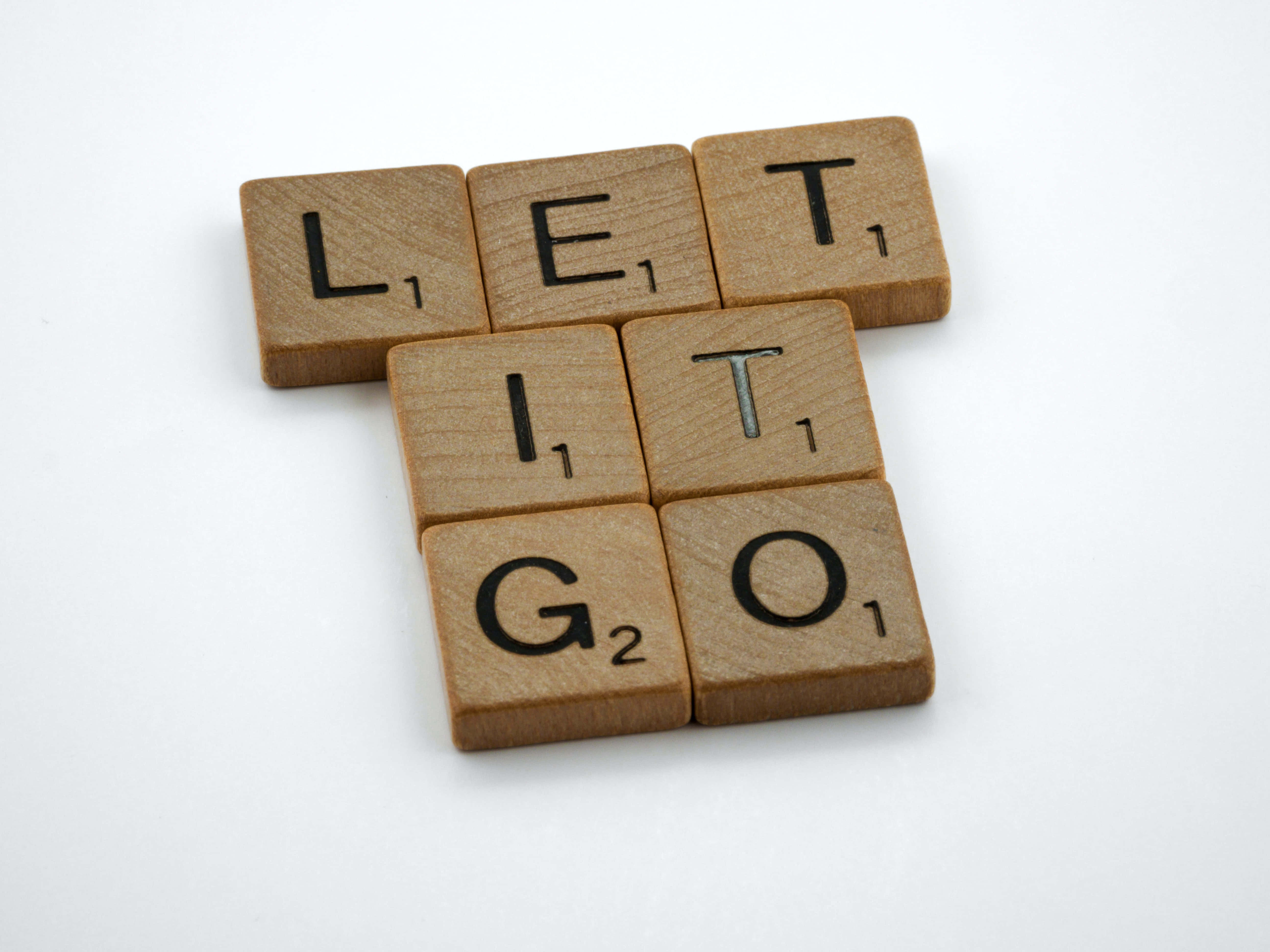 激勵性拼字遊戲藝術 - 「Let It Go」 壁紙 — 木製 Scrabble 字母塊拼出 LET IT GO，以 T 形排列在純白色背景上。