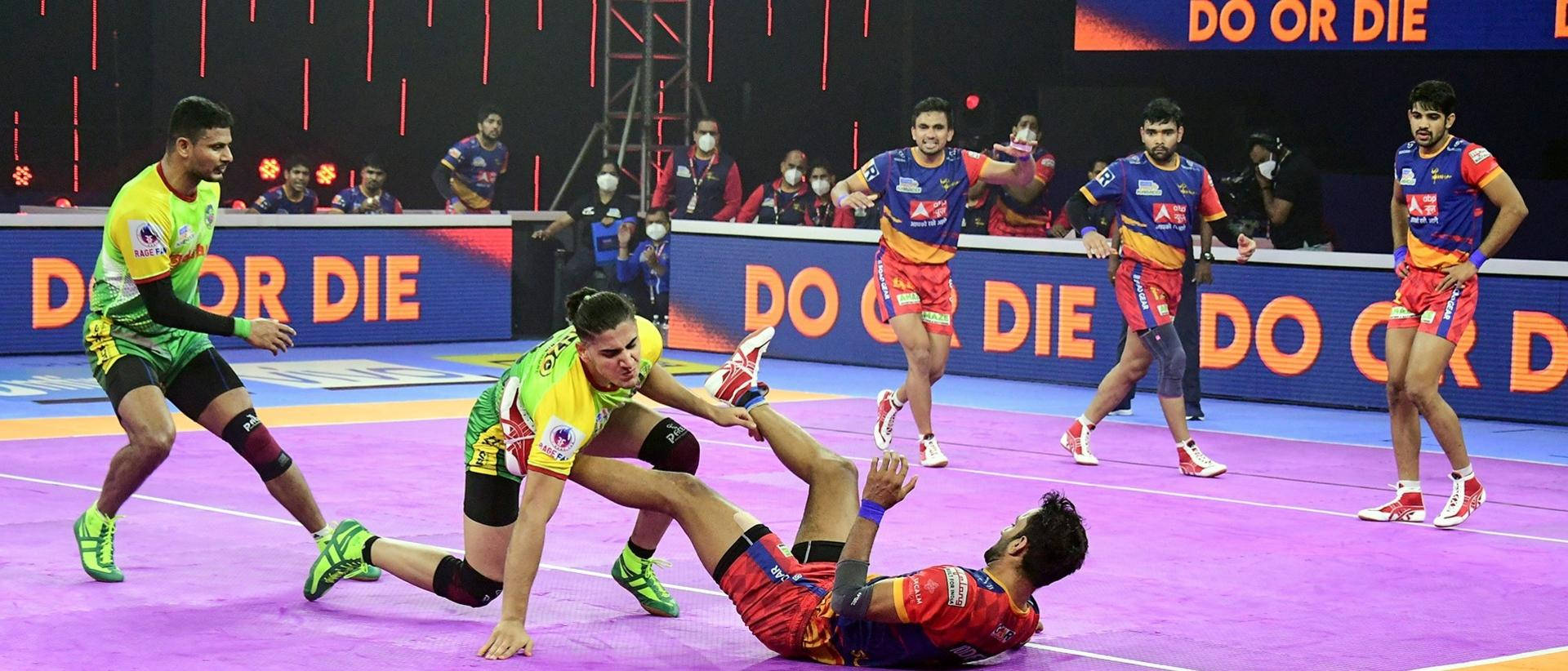 兩名身穿綠色和紅色球衣的板式網球運動員在紫色球場上激烈競爭。