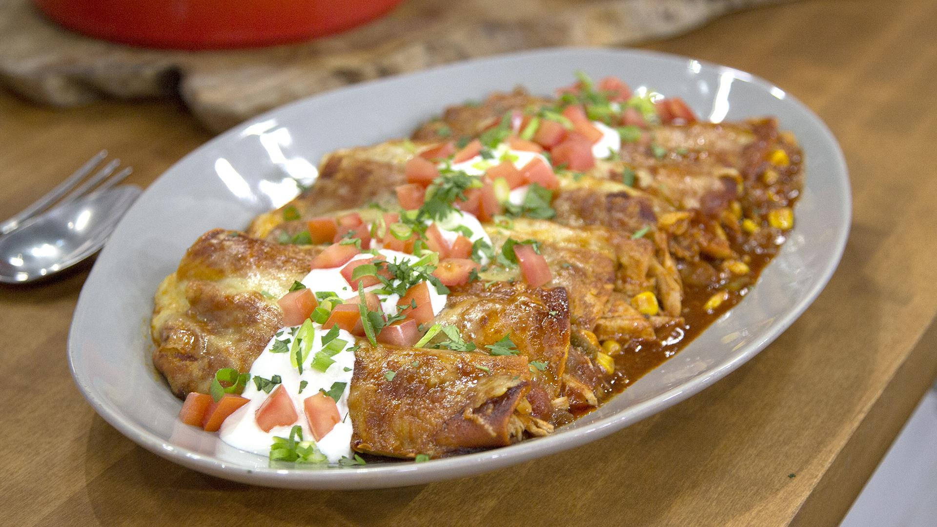 濃郁奶油 enchiladas 盤中盛放 壁紙 — 一盤金黃色的玉米捲餅，浸在紅醬中，上面鋪上新鮮番茄、酸奶油和香菜。