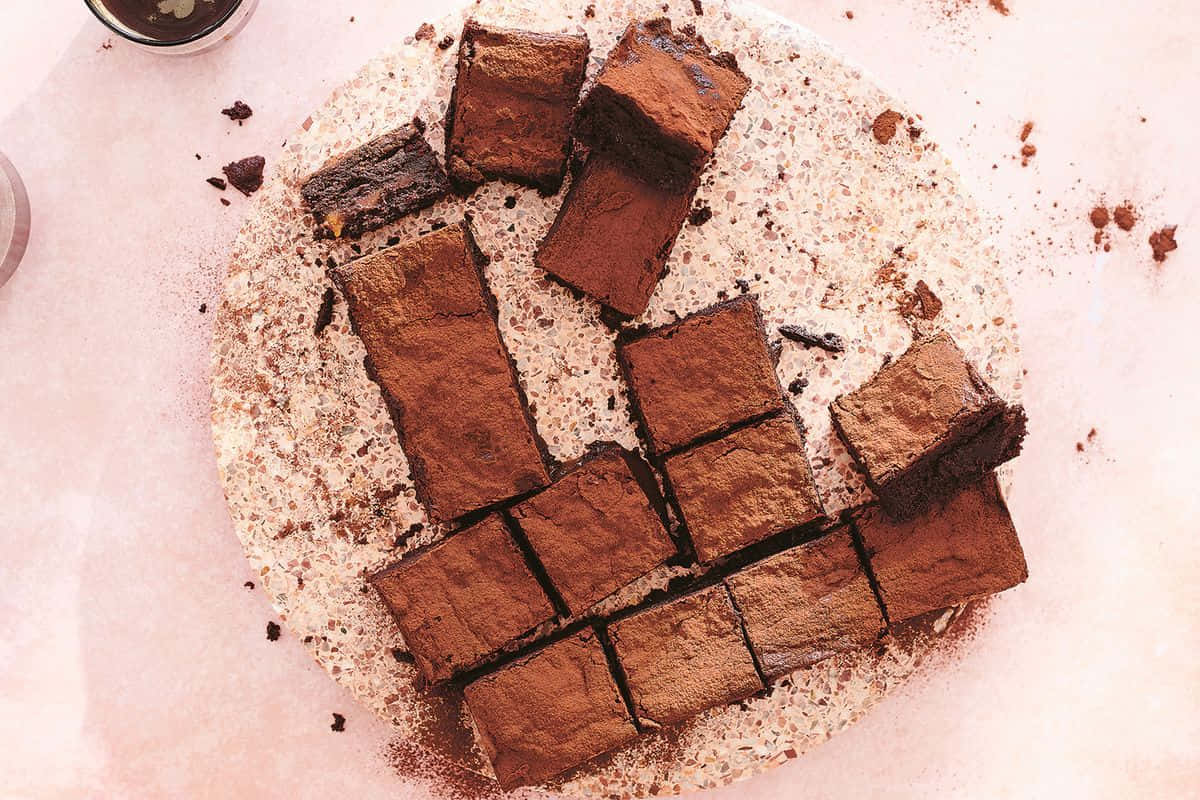 Caramel Brownie 桌布 壁紙 — 濃郁的朱古力布朗尼切成方塊，放在撒有可可粉的斑點盤上。