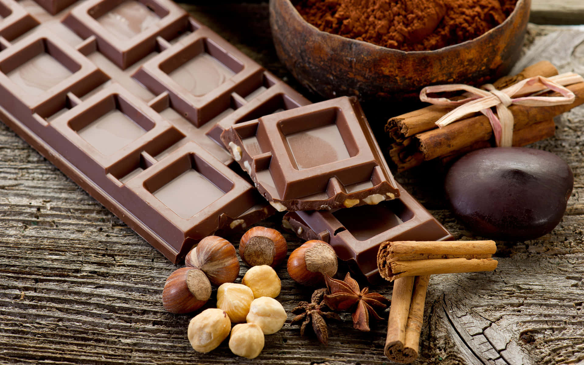 Brown Chocolate 桌布 壁紙 — 濃郁的朱古力條和肉桂、榛子等香料放在經風化的木質表面上。