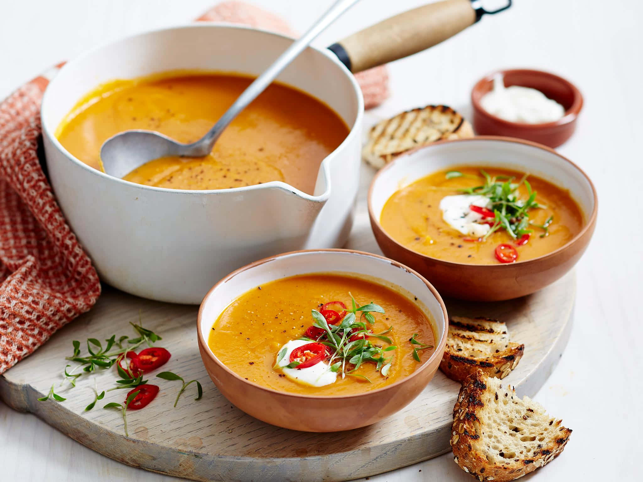 Soup 桌布 壁紙 — 濃郁的橙色湯盛在陶碗中，配上酸奶油、辣椒和香草，放在木板上。