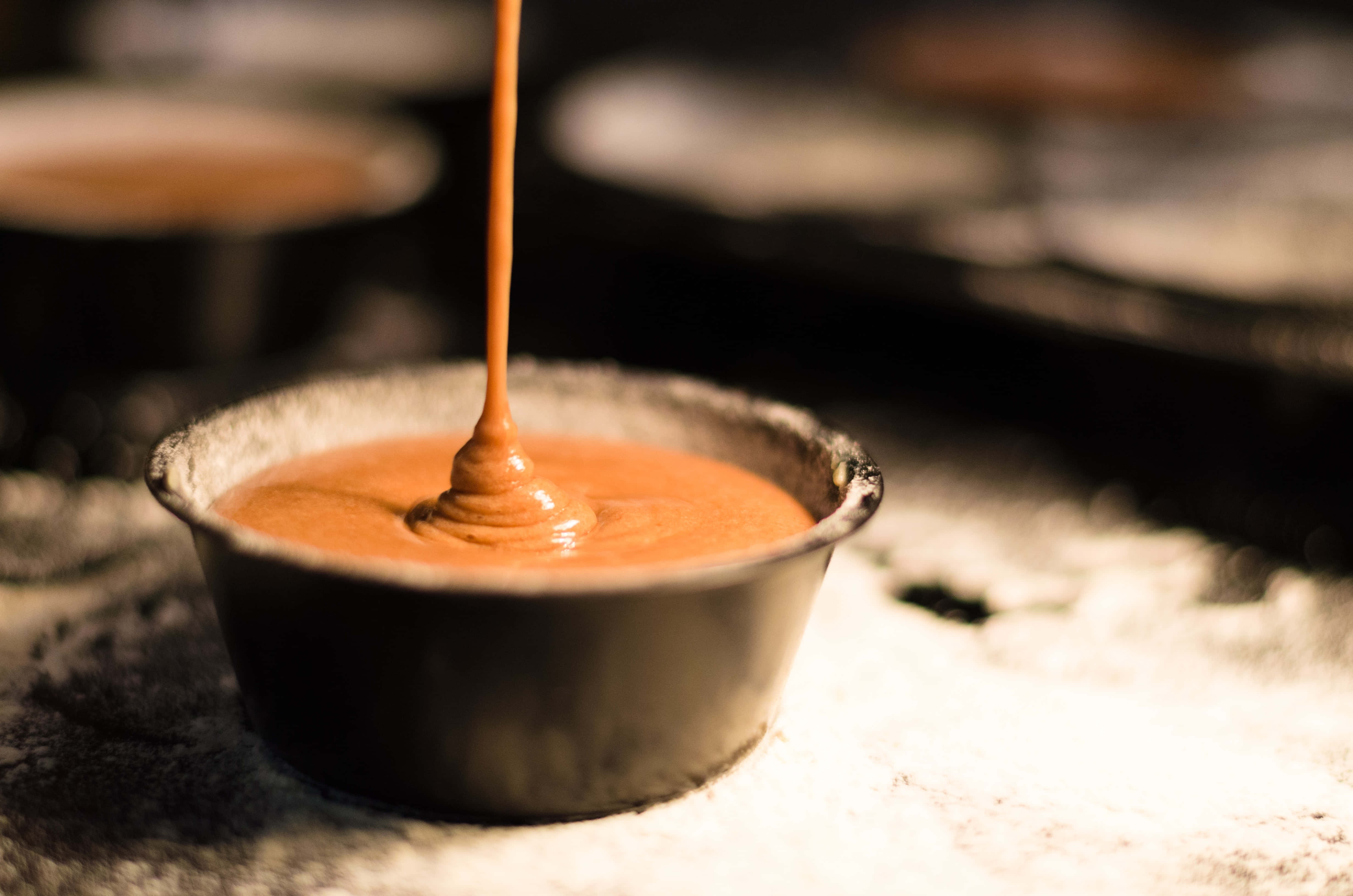 Caramel 桌布 壁紙 — 濃郁的焦糖醬以濃稠的流柱倒入撒有糖粉的深色小烤碗中。