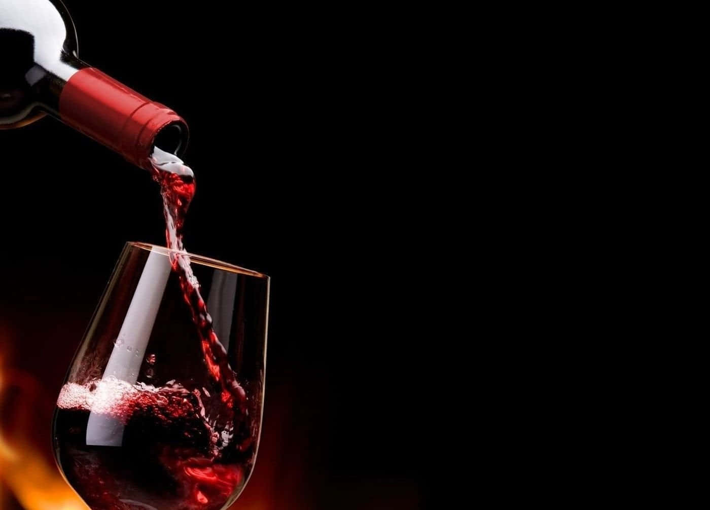 Red Wine Glass 桌布 壁紙 — 濃郁的紅酒從酒瓶倒入玻璃杯中，背景昏暗，下方有溫暖發光的光線。