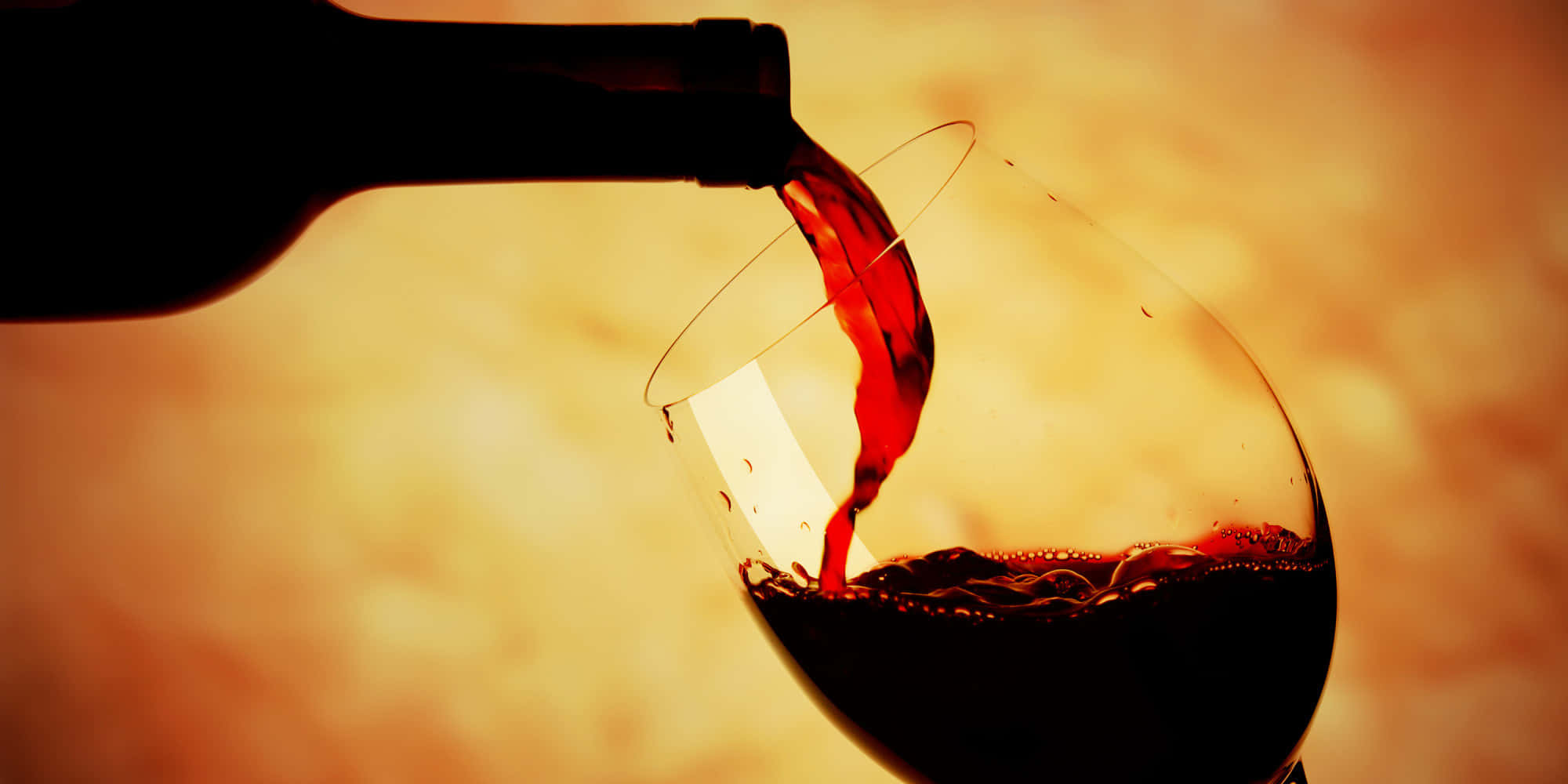 Black Wine 桌布 壁紙 — 濃郁的紅酒從酒瓶倒入玻璃杯中，背景是溫暖的金色。