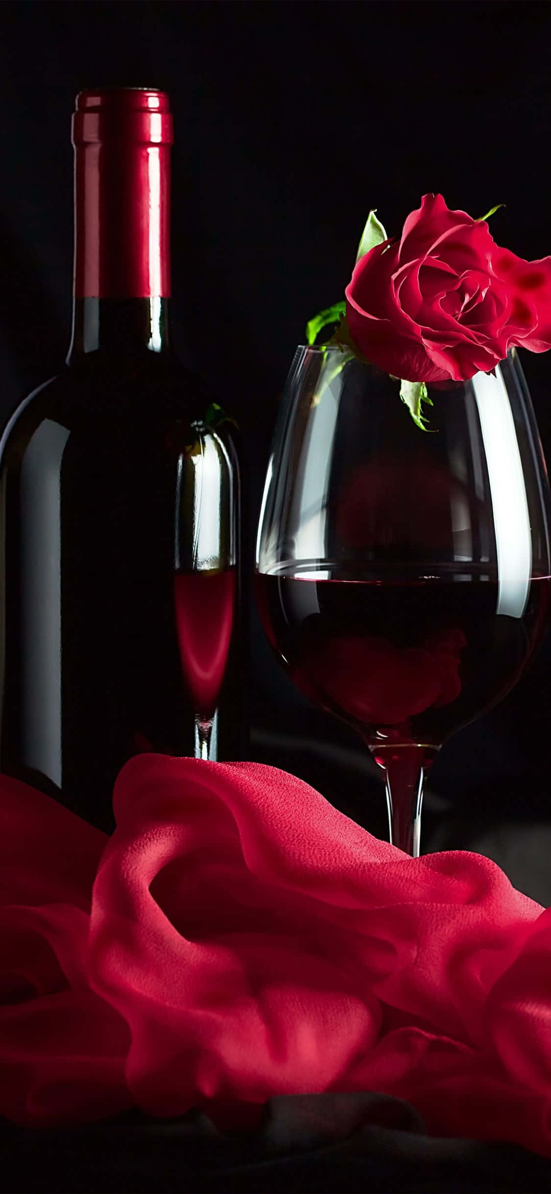 Red Wine Glass 桌布 壁紙 — 濃郁的紅酒瓶和酒杯，配以玫瑰和絲綢布料，在深色背景下呈現。