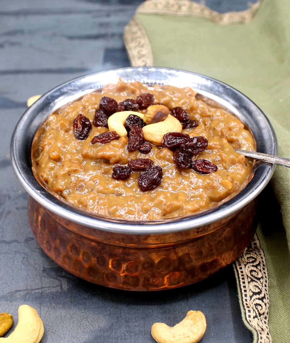 Pongal 桌布 壁紙 — 濃郁的金黃色kheer，上面放有提子乾和腰果，盛載於錘紋銅碗中，置於深色石板表面上。