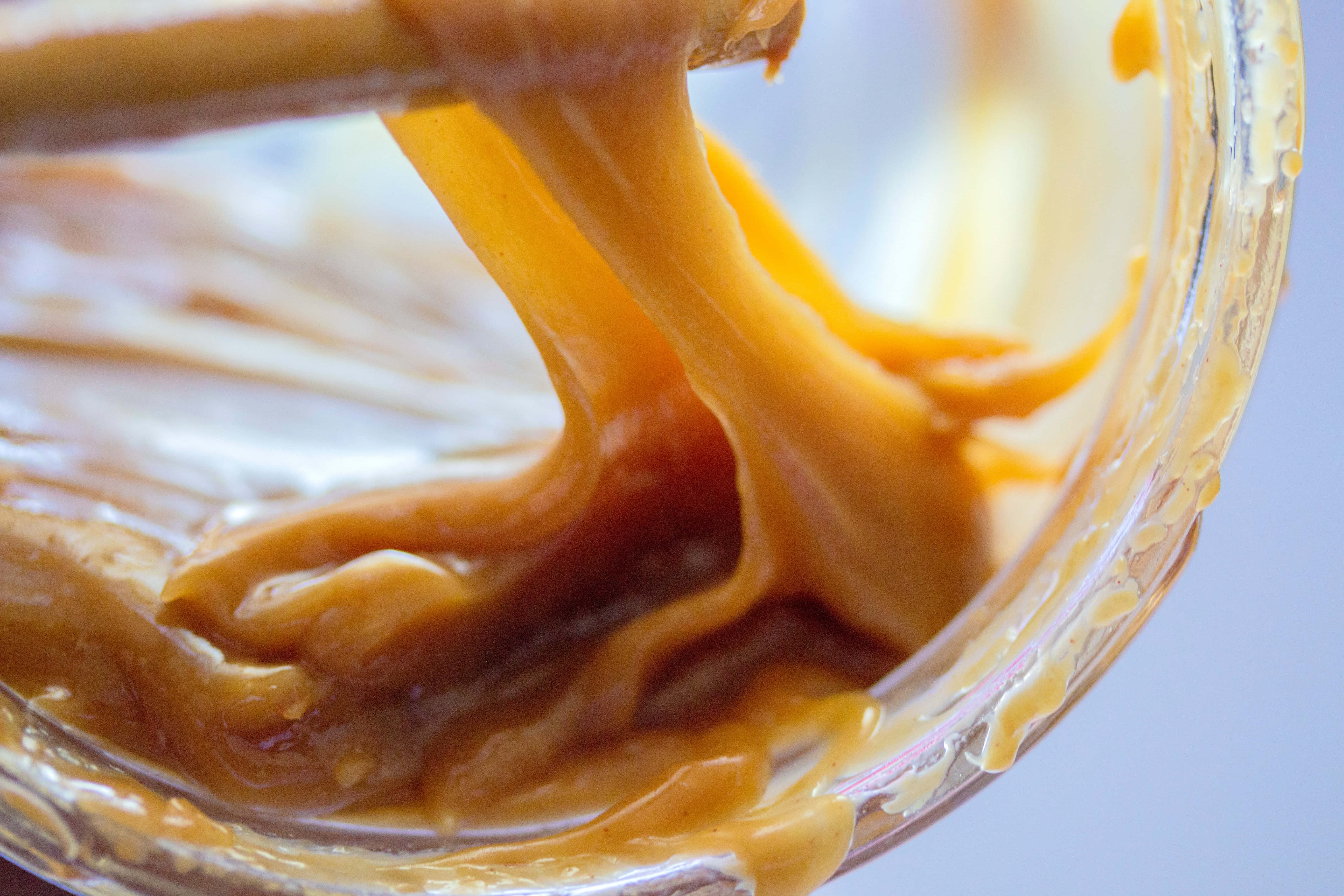 Caramel 桌布 壁紙 — 濃郁的金黃色焦糖醬在慢動作中從玻璃碗中用木勺提起時拉伸。