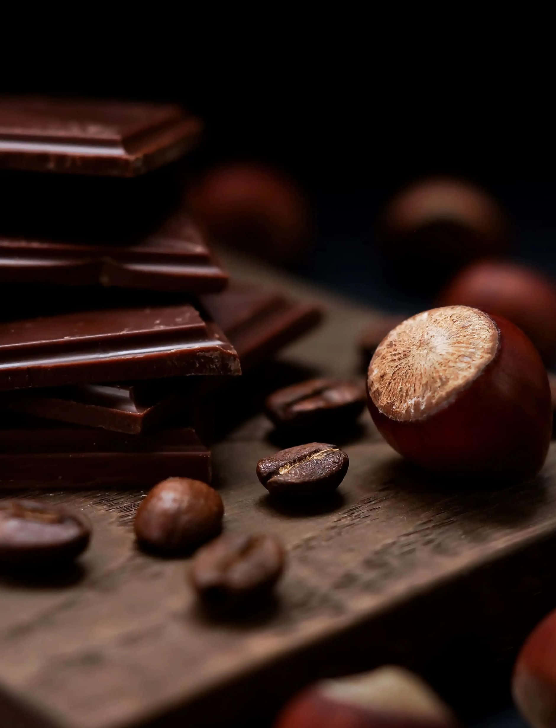 Dark Chocolate 桌布 壁紙 — 濃郁的黑朱古力條、咖啡豆和榛子排列在質樸的木質表面上，帶有深沉的陰影。