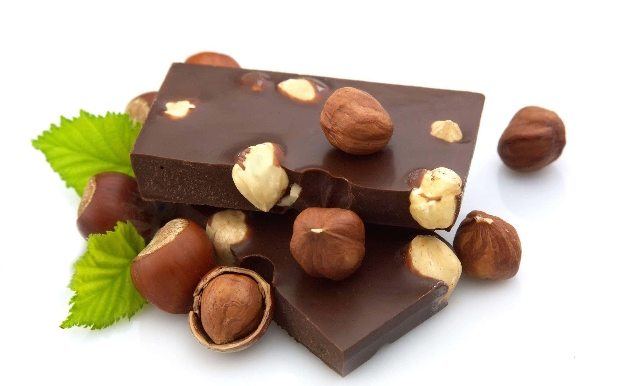 Brown Chocolate 桌布 壁紙 — 濃郁黑朱古力條，綴以完整及碎裂的榛子和新鮮綠葉，置於白色背景上。