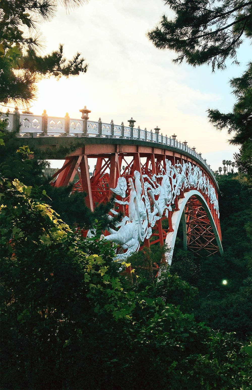 濟州島仙人橋 壁紙 — 一座引人注目的紅色拱橋，帶有白色龍雕塑，在金色日落時蜿蜒穿過茂密的綠樹。