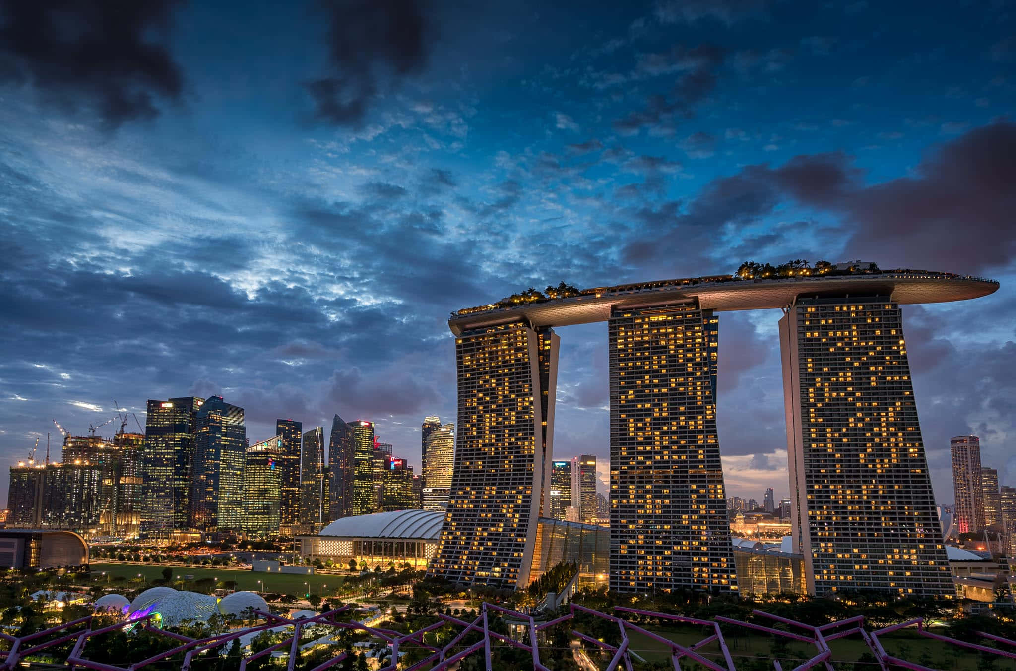 Asia 桌布 壁紙 — 濱海灣金沙的塔樓在新加坡天際線上，在佈滿散雲的戲劇性暮色天空中溫暖地發光。