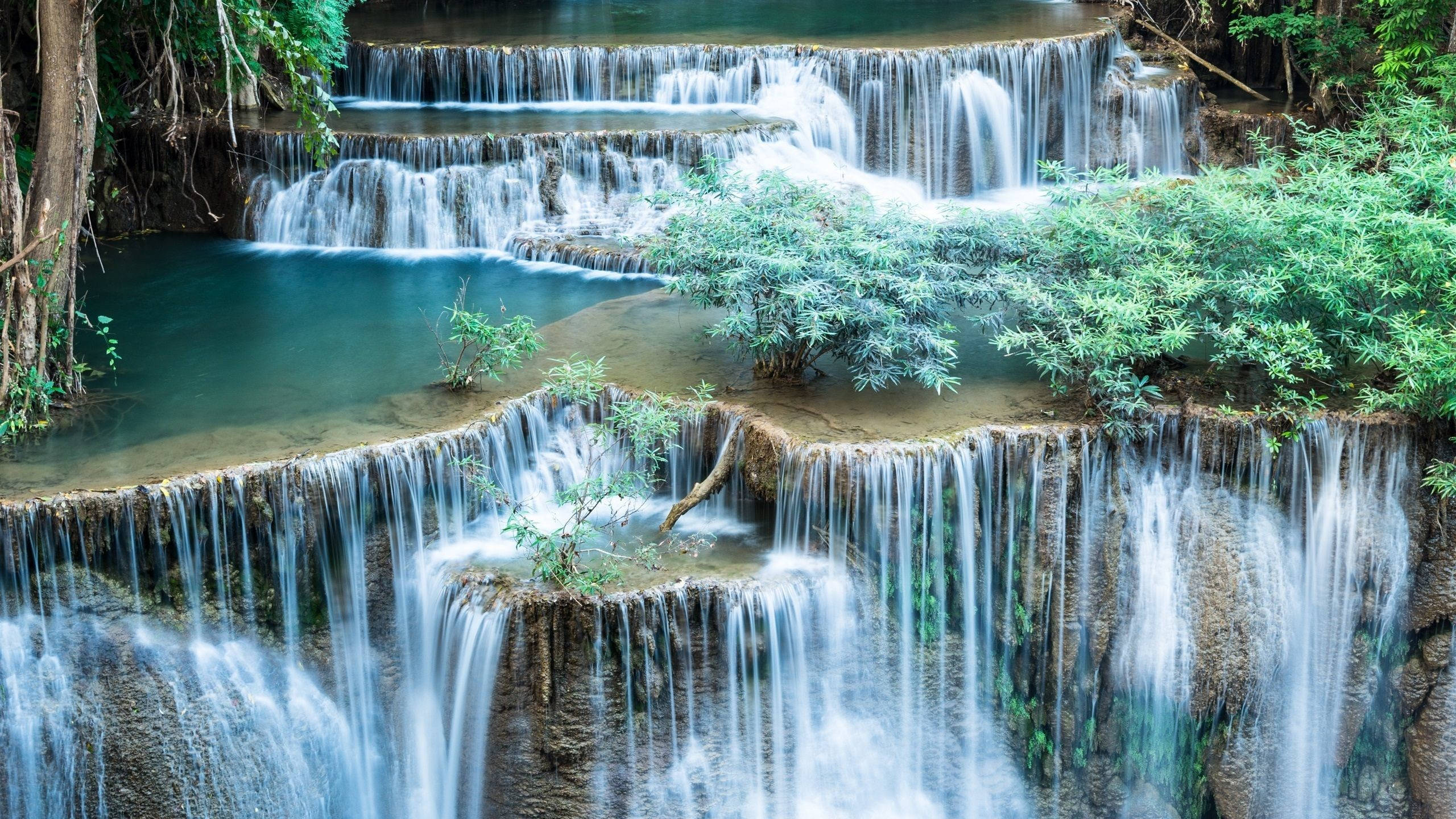瀑布風景 壁紙 — 一個寧靜的多層瀑布流經茂密的綠色叢林，有藍綠色水池和長滿苔蘚的岩石。